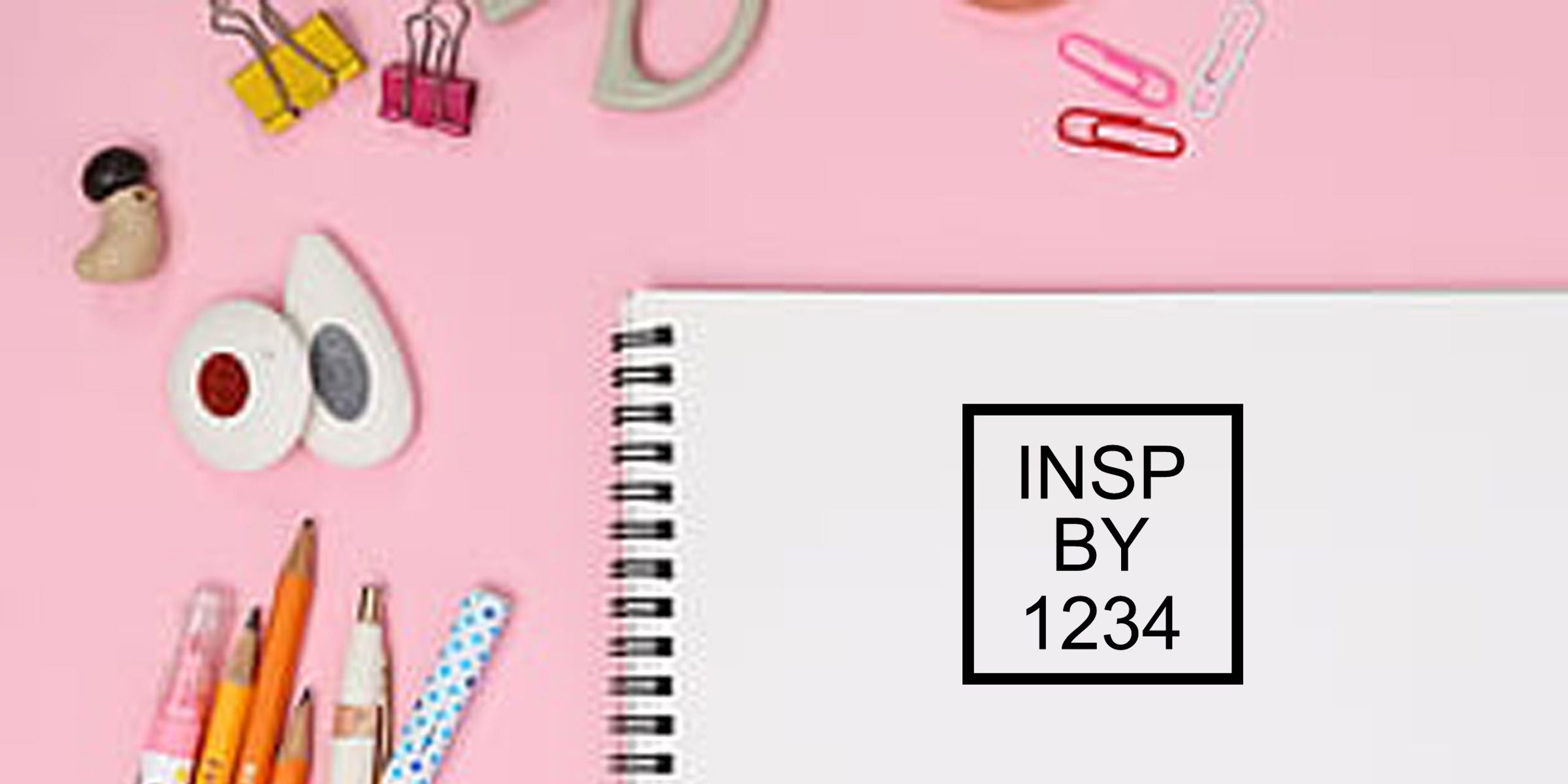 Pink stationery flat lay with spiral notebook, pencils, binder clips, paper clips, and “INSP BY 1234” text on a white notebook cover
