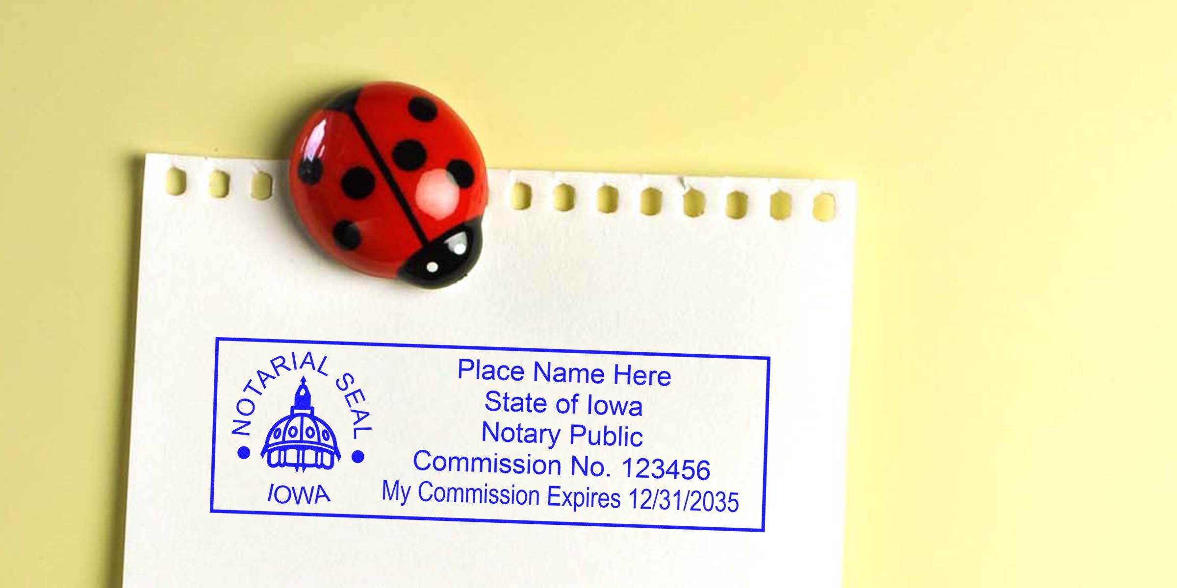 Iowa notary stamp with commission number and expiration date on white paper, held by ladybug magnet; purchase your notary stamp online today.
