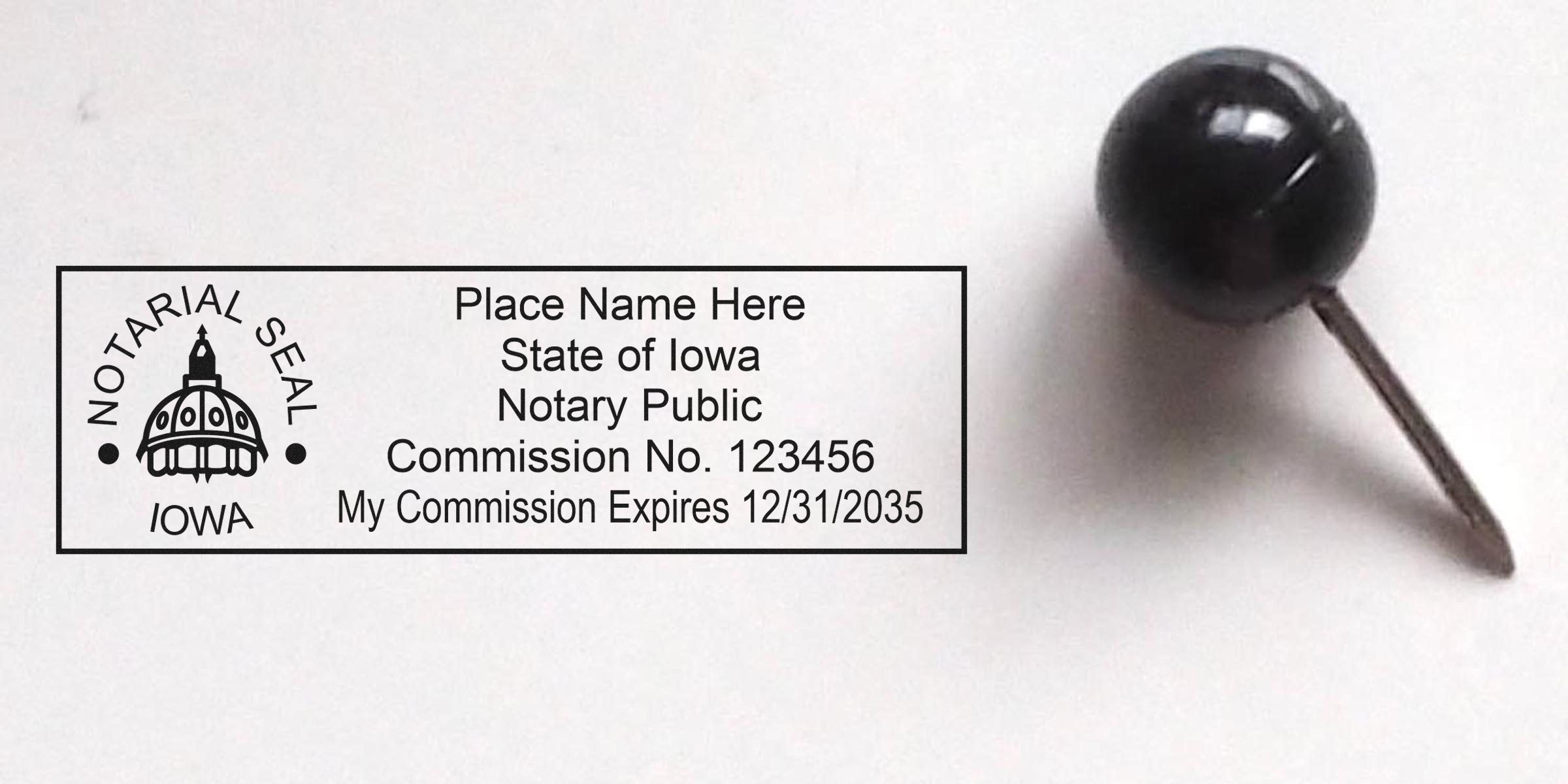 Iowa notary public stamp with commission number and expiration date beside a black push pin on a white background, part of essential notary supplies in an Iowa notary kit.