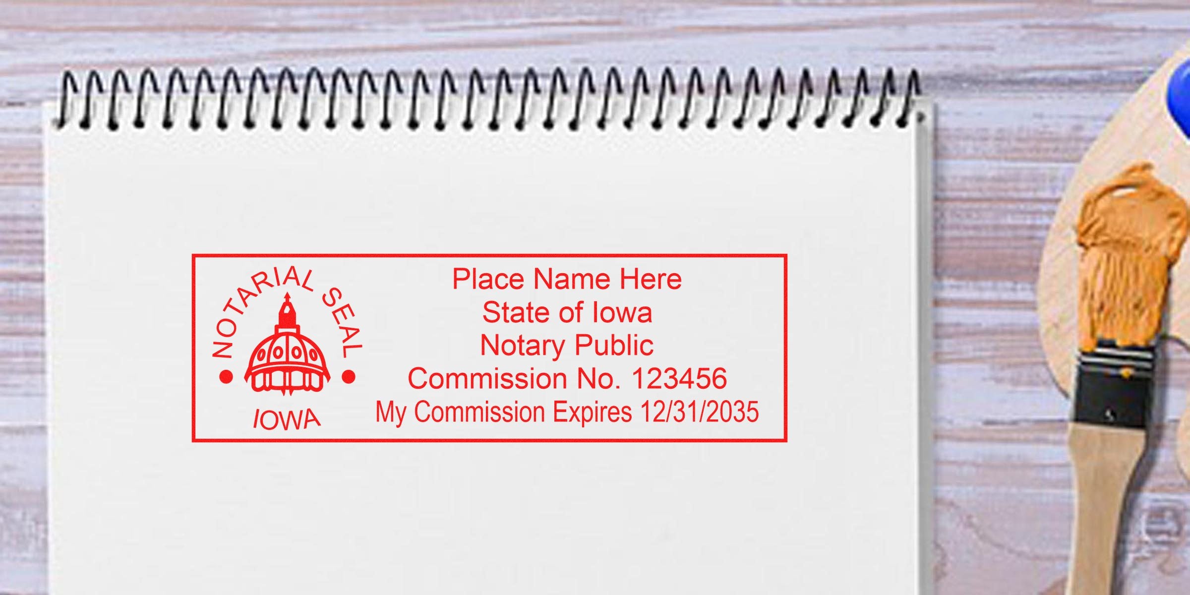 Iowa notary public stamp on white notepad with commission number and expiration date, next to paintbrush and palette, showing Iowa notary seal size and dimensions.