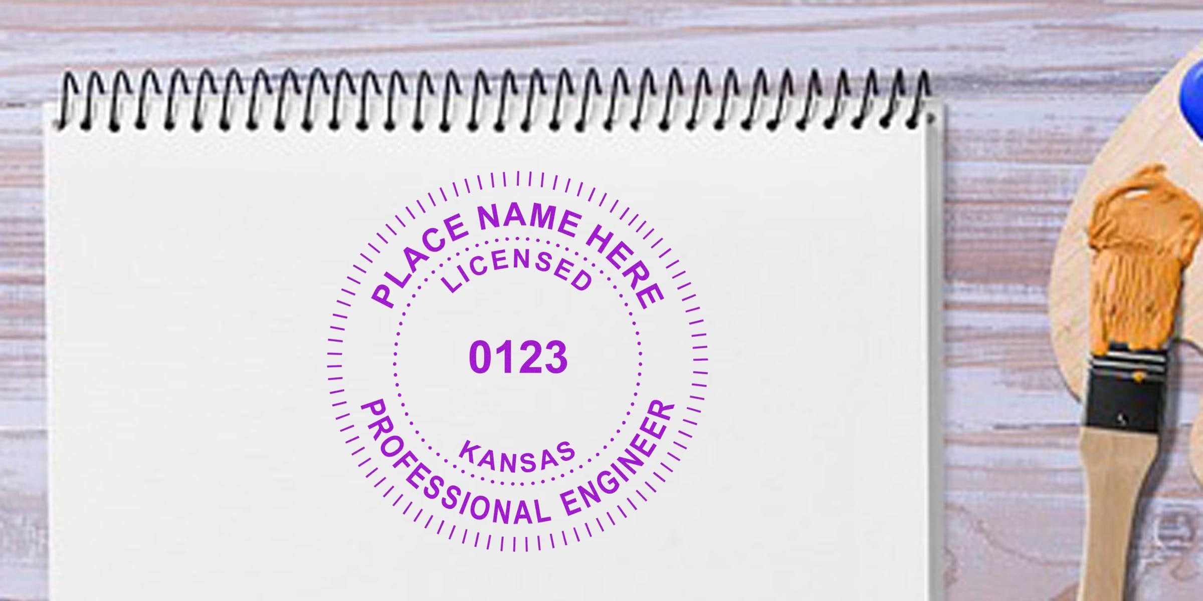 Kansas engineer stamps with a professional engineer license stamp and paintbrush on a wooden table, offered by trusted engineer stamp suppliers.