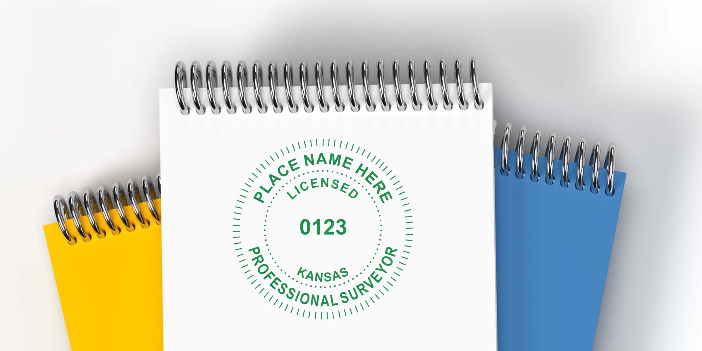 Kansas land surveyor seal stamped on white spiral notebook, with yellow and blue notebooks behind, showing land surveyor seal design checklist.