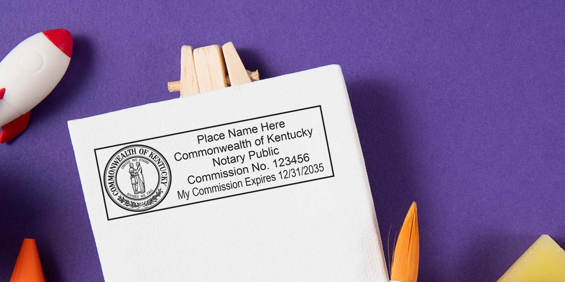 Kentucky notary stamp with commission number and expiration date on white paper, surrounded by art supplies, emphasizing Kentucky notary stamp renewal and renewal requirements.