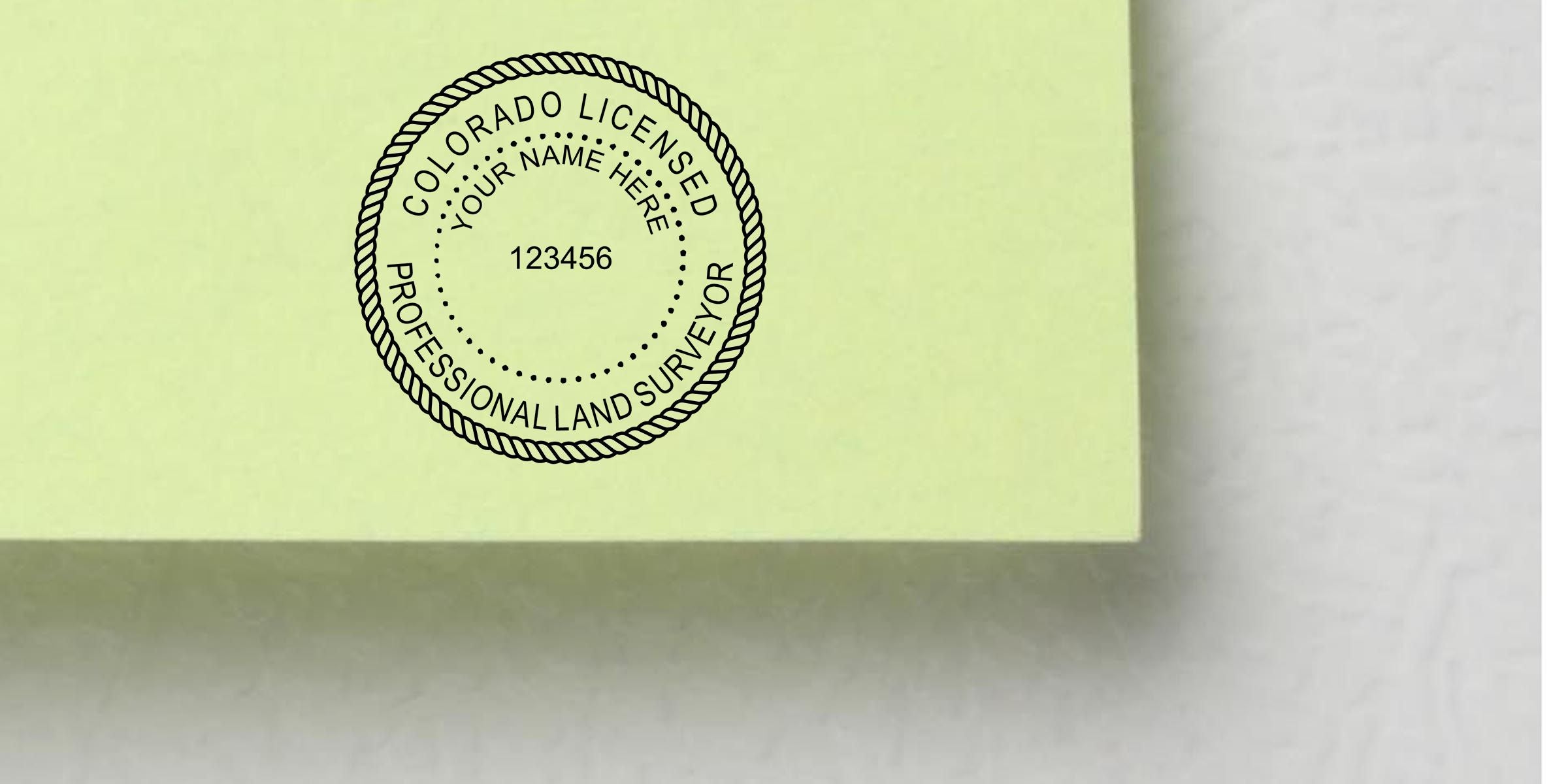 Close-up of a Colorado licensed professional land surveyor stamp on a pale yellow document with placeholder name and license number 123456