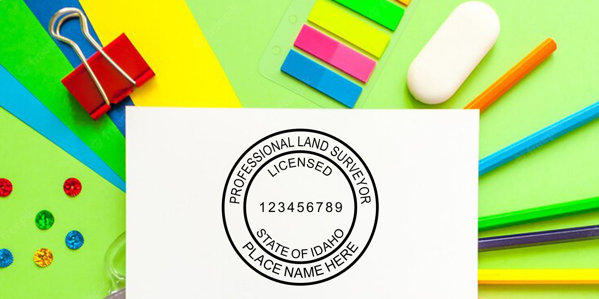 Professional land surveyor licensed state of Idaho stamp on white paper with colorful office supplies, sticky notes, binder clip, and pencils background