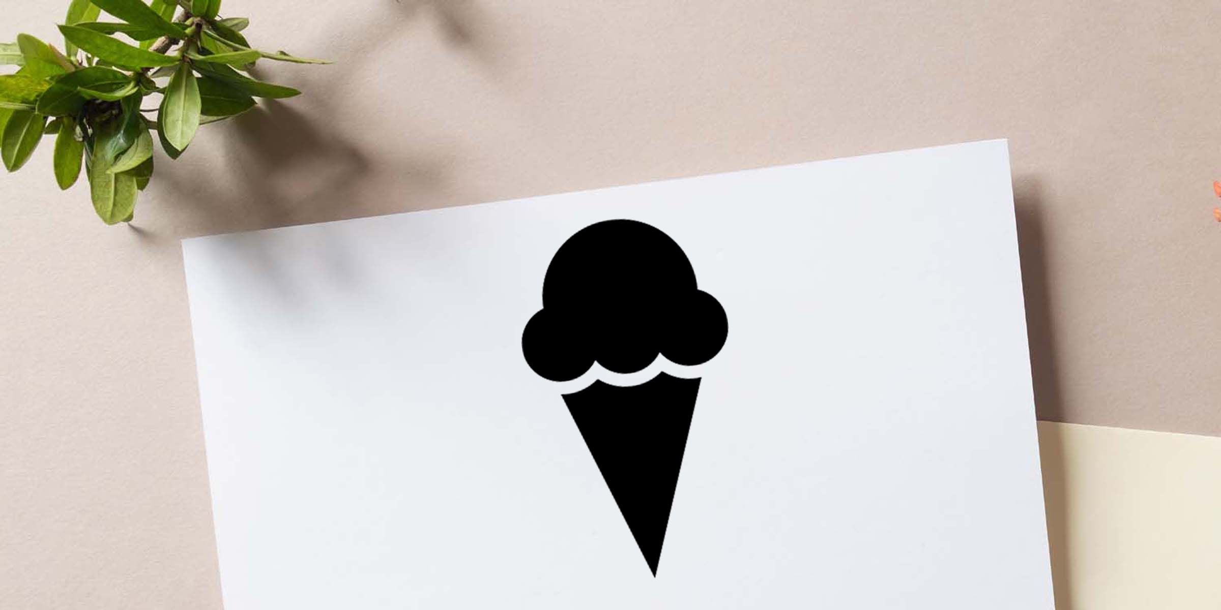 Black ice cream cone icon on white paper with green leaves on a beige tabletop background
