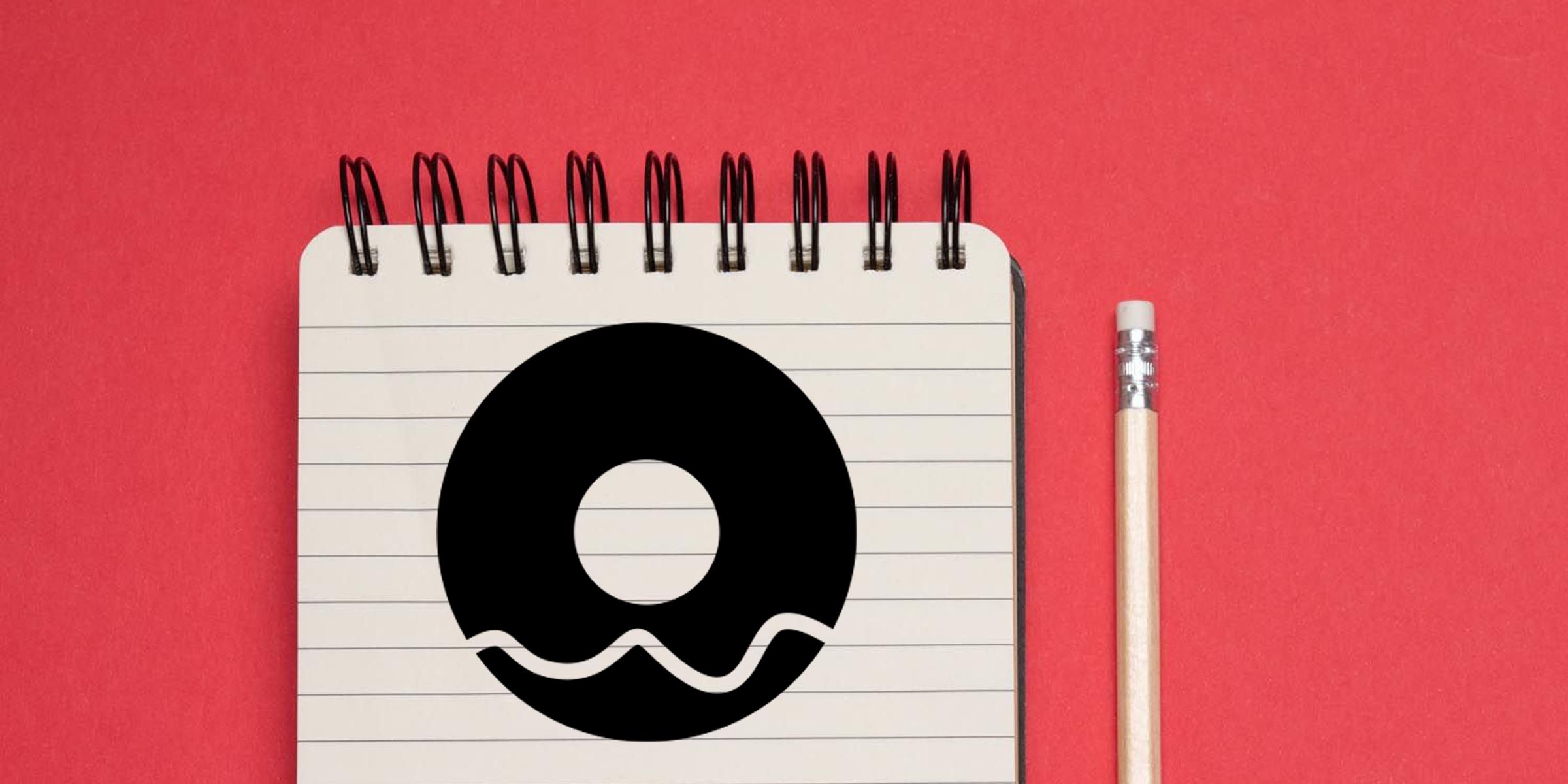 Spiral notebook with bold black Q logo and pencil on red background