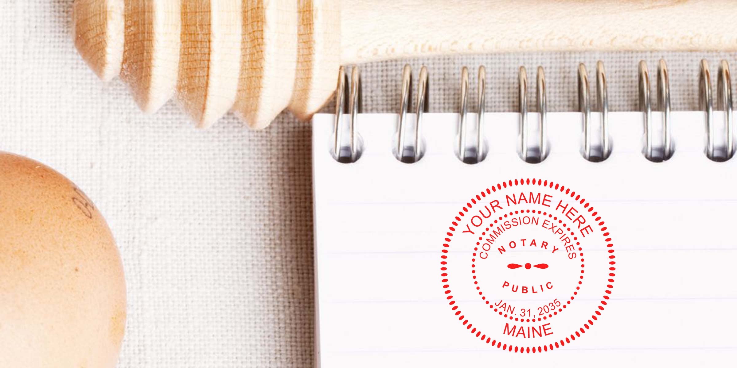 Maine notary seal stamp on spiral notebook with notary public stamp, wooden honey dipper, and egg on linen, showing Maine notary commission expiration date and trusted notary supplies.