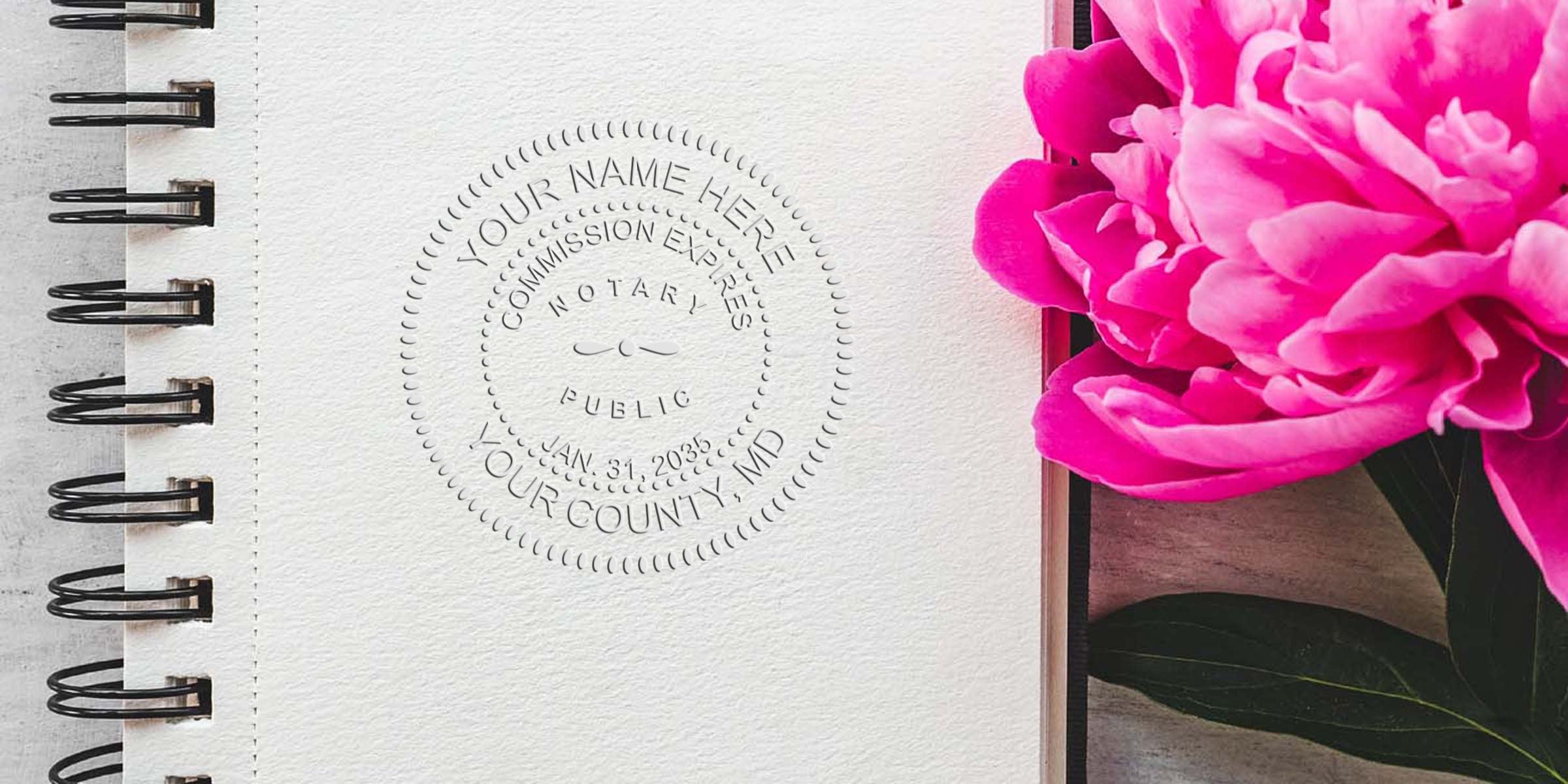 Spiral notebook with Maryland notary embossed seal, vibrant pink peony, and self-inking notary stamp on wooden table.