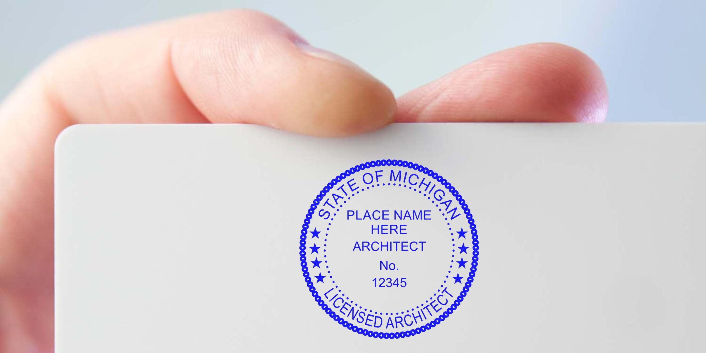 Hand holding Michigan architect stamp showing license number and name, meeting Michigan architect stamp requirements.