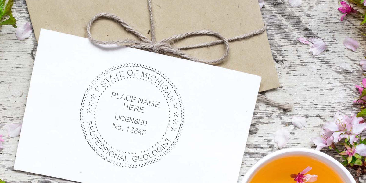 Professional geologist license seal with Michigan design on white paper, alongside a rustic envelope and floral teacup on a wooden table.