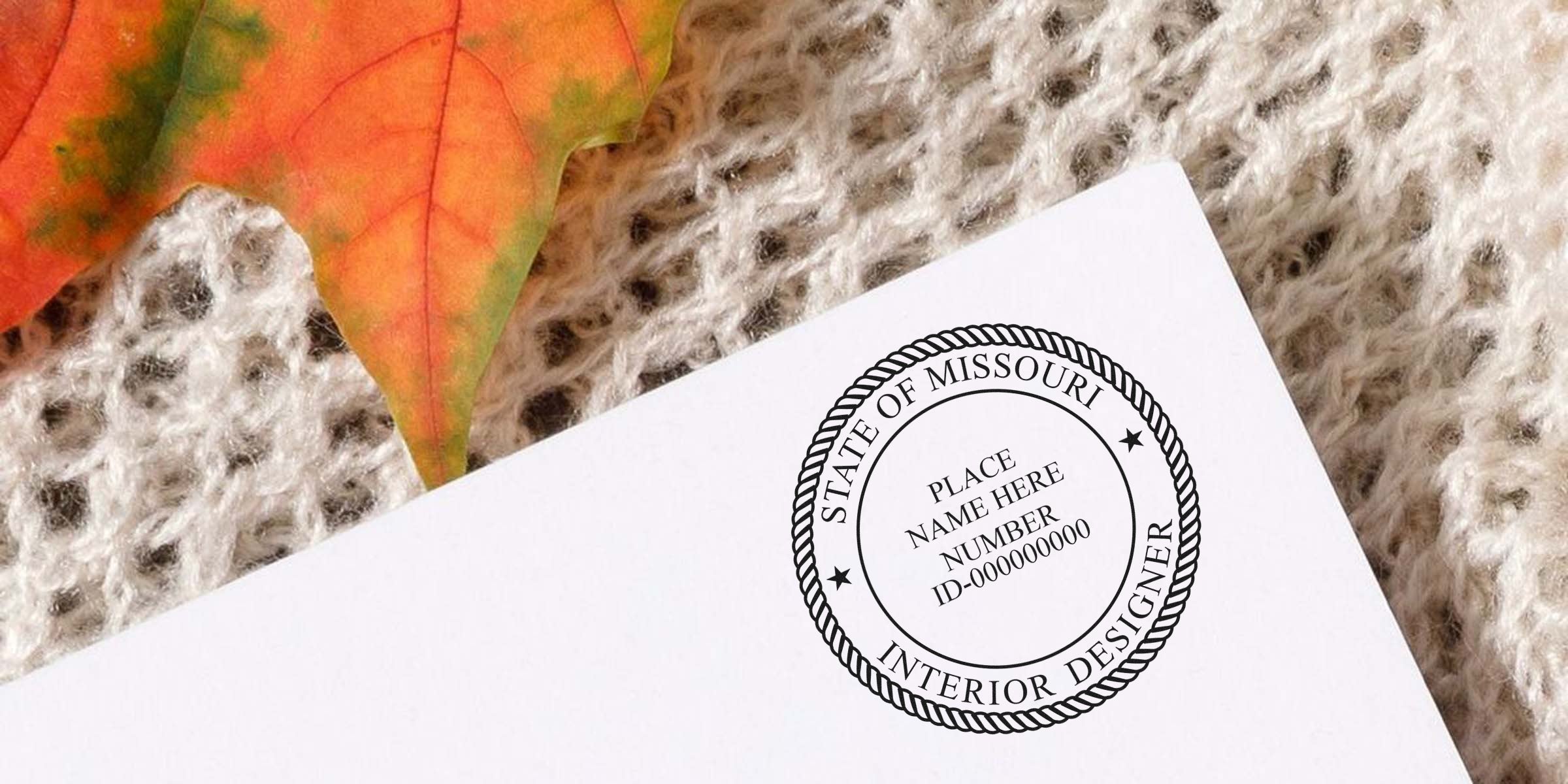 Missouri interior designer certification seal on white paper with autumn leaf and knitted fabric background, showing Missouri interior designer stamp; purchase interior designer stamp online.