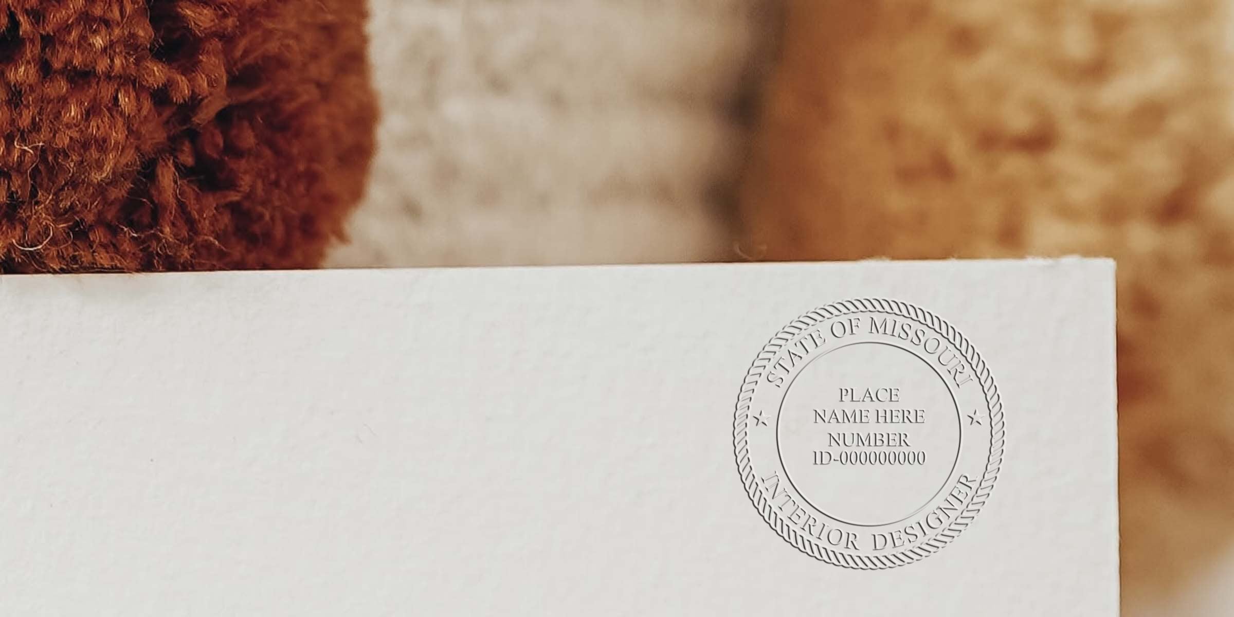 Close-up of a white certificate with an embossed Missouri interior designer stamp next to textured brown and beige fabric, showcasing compliance with Missouri interior design stamp requirements.