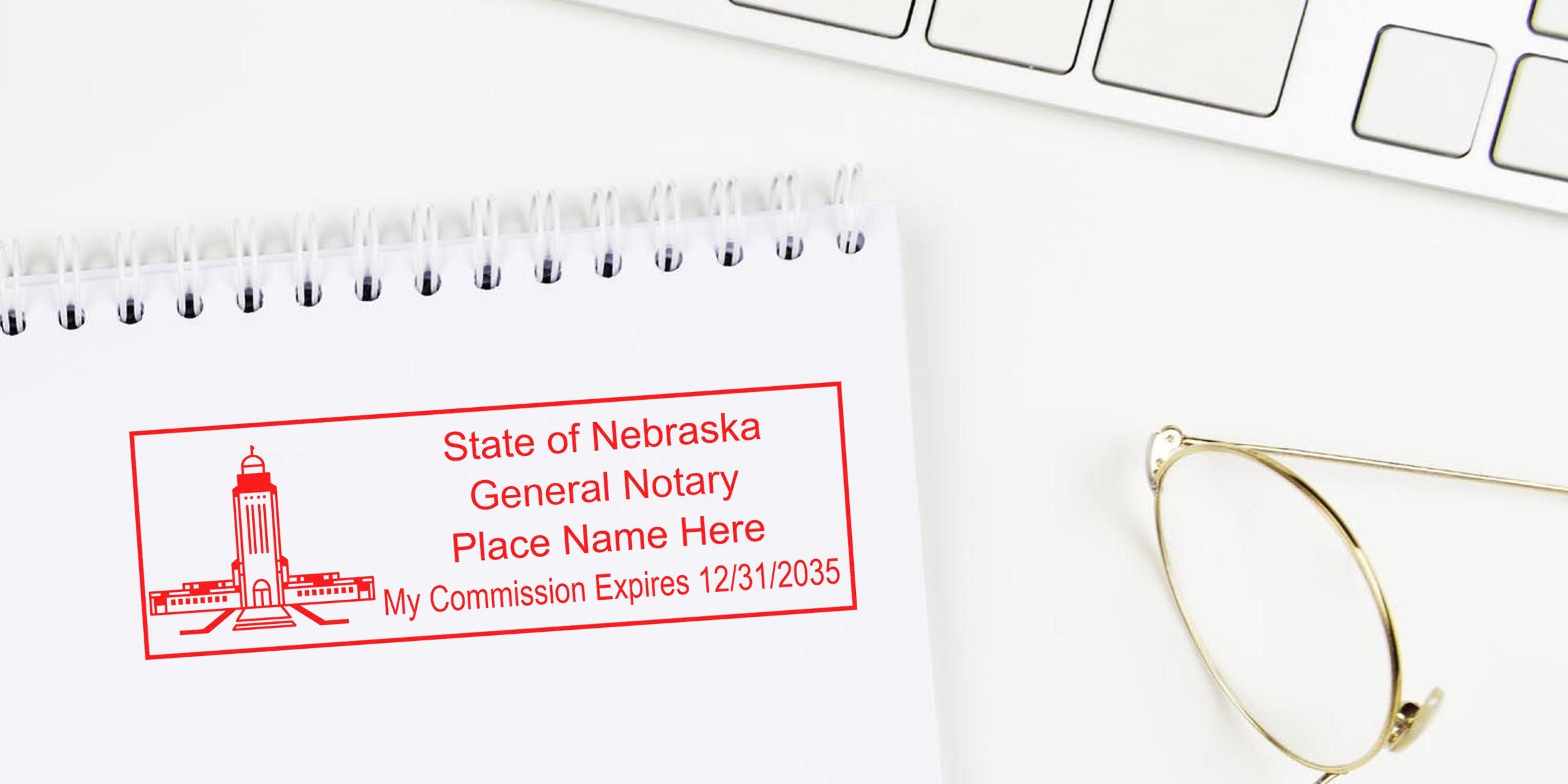 Nebraska notary stamps on a white spiral notebook with gold glasses and keyboard, highlighting essential notary public supplies in Nebraska.