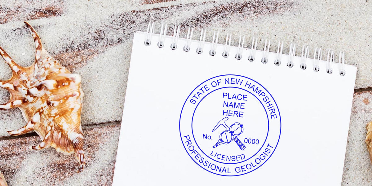 New Hampshire geologist stamp on white notepad with seashells on sandy wood, revealing stamp design secrets.