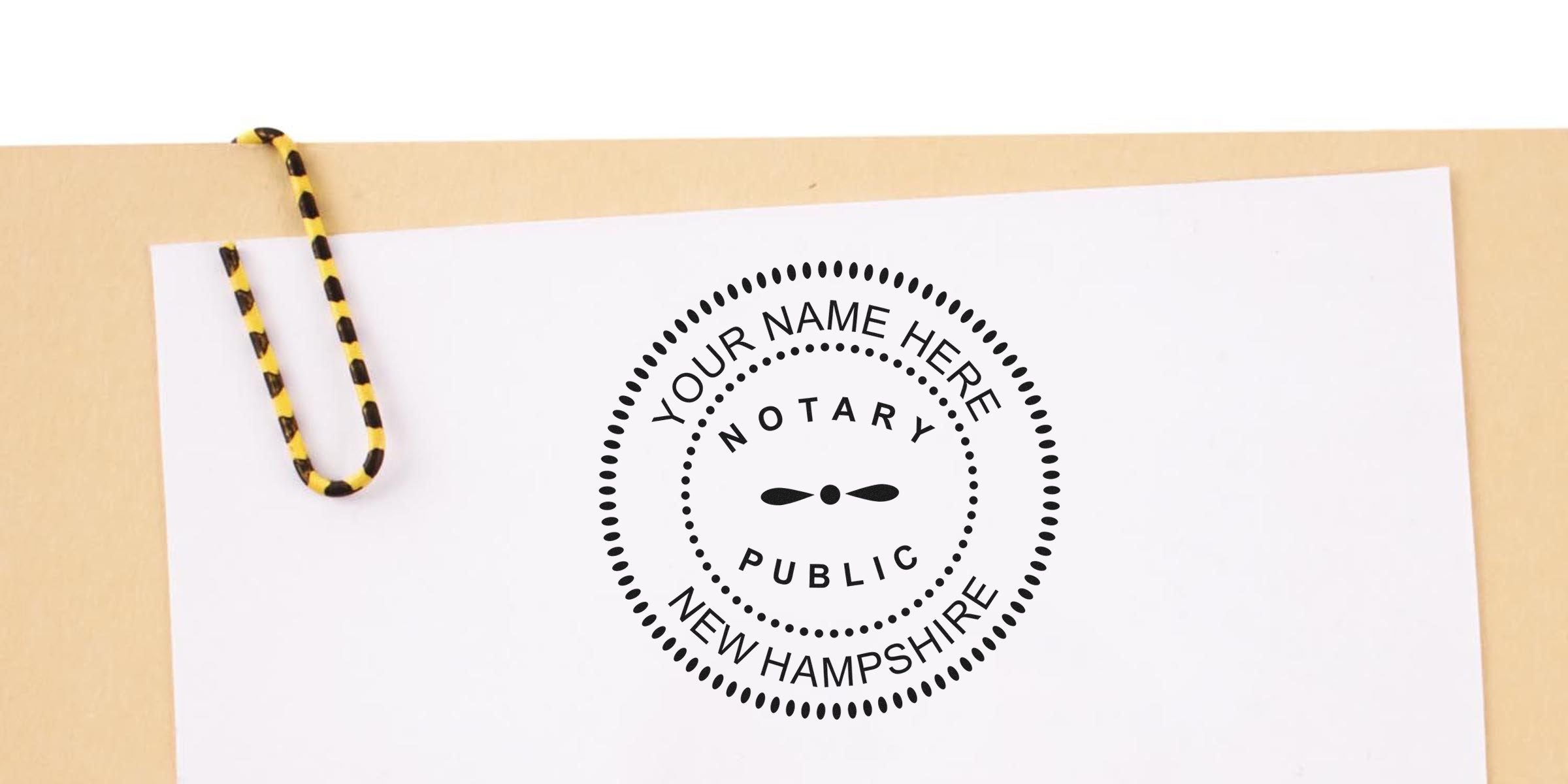 Self-inking New Hampshire notary stamp with yellow and black paperclip on beige background.