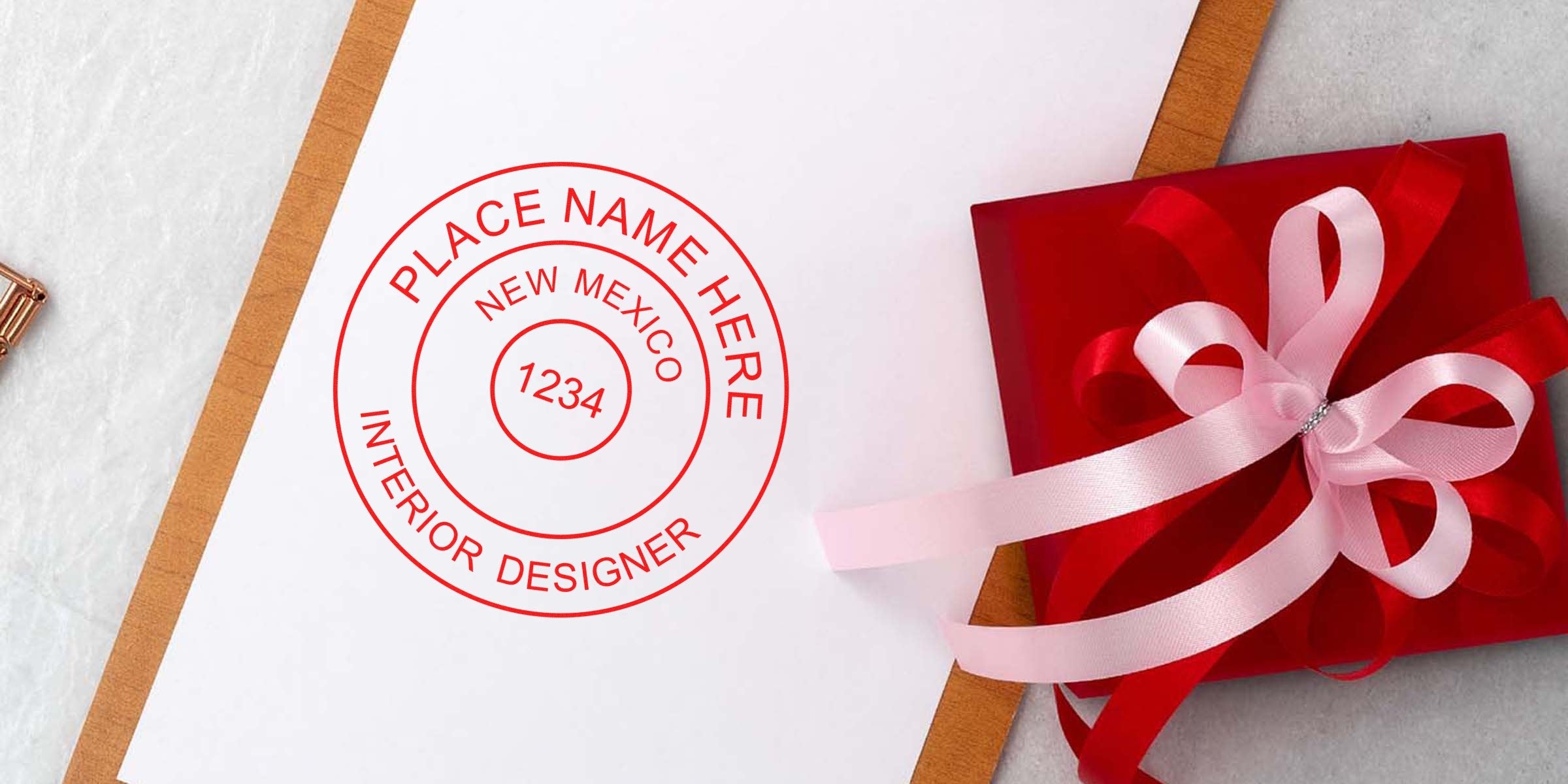 Red gift box with pink ribbon next to New Mexico Interior Designer Seal on white paper, showing the Official Interior Designer Certification NM.