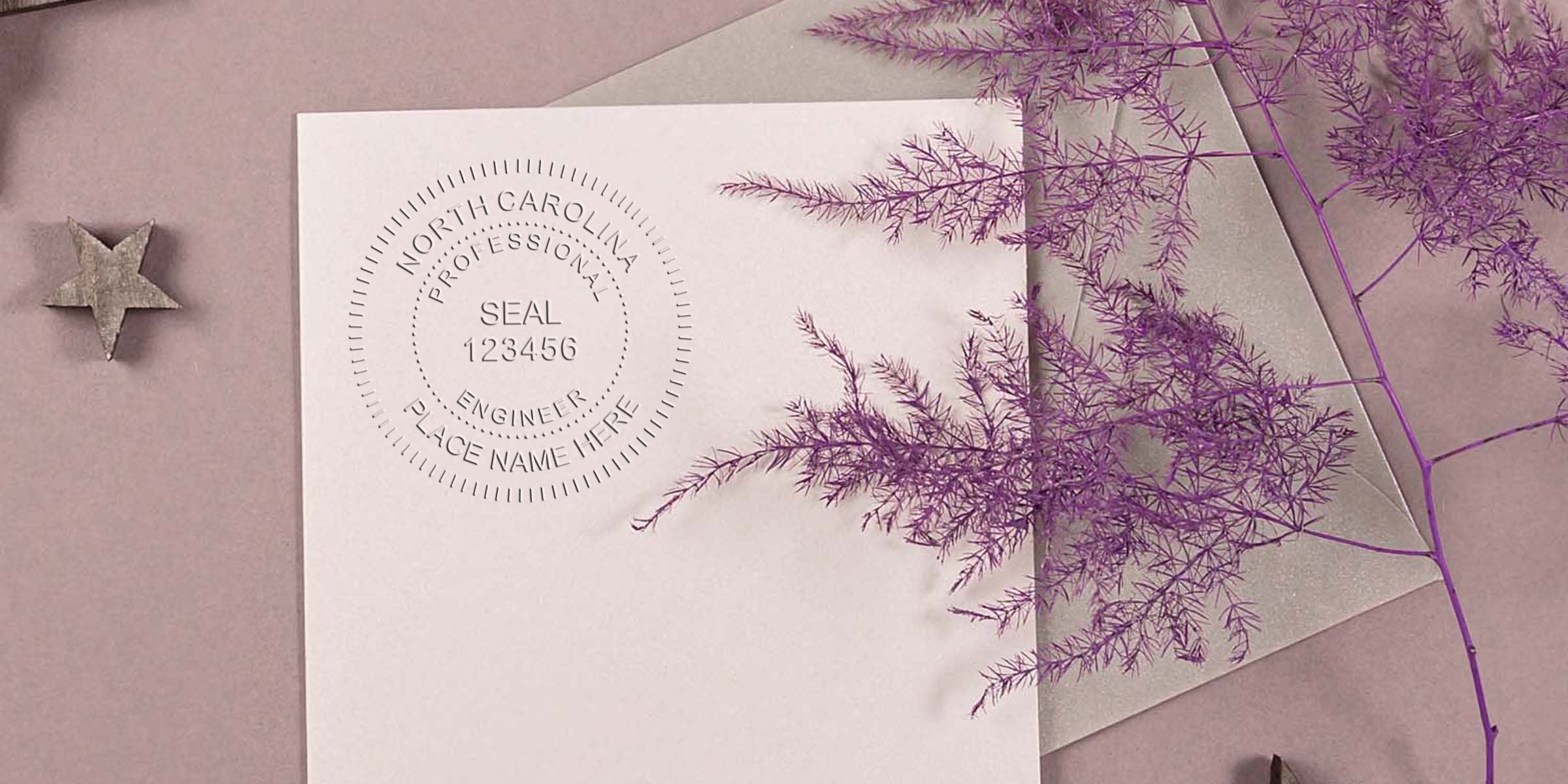 North Carolina engineer seal embossed on white paper with purple fern design, silver envelope on pink background, made using engineer seal embossers.
