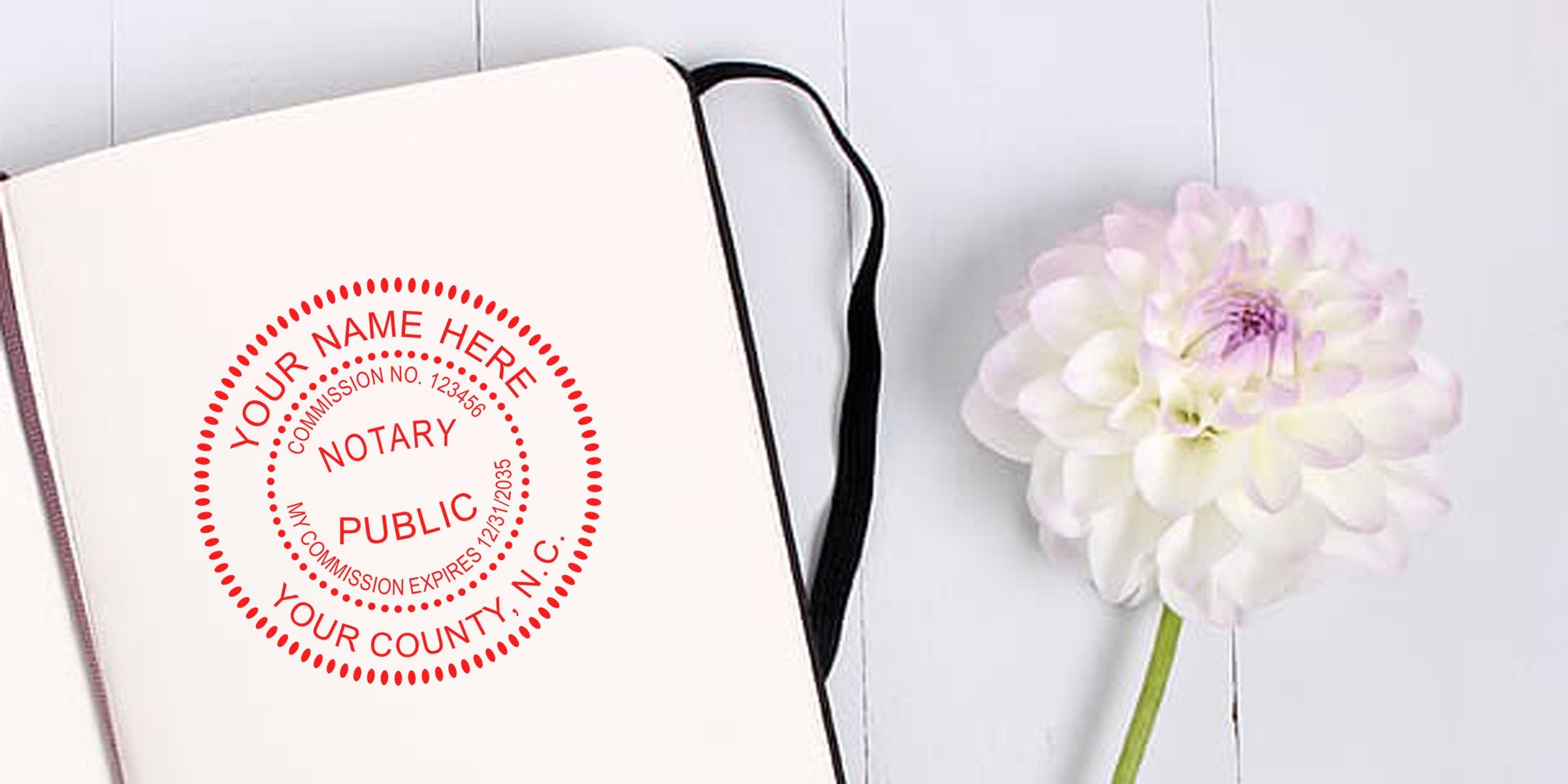 Notary stamp from North Carolina on an open notebook with a flower, set on a white wooden background, highlighting tips for buying a notary stamp.