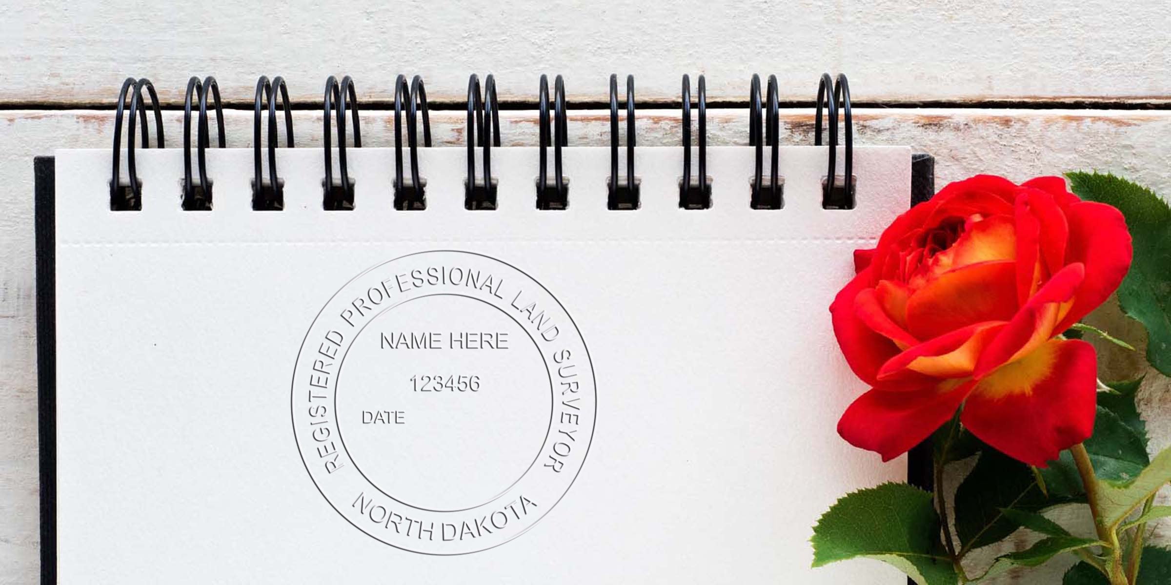 Registered professional land surveyor stamp with North Dakota surveyor seal on notebook, accompanied by a red rose, highlighting the surveyor seal design.