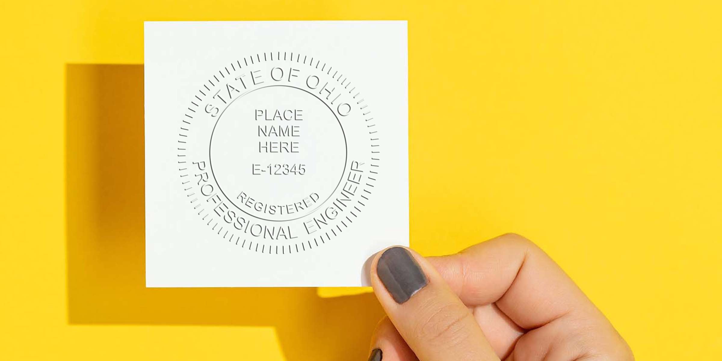 Hand holding Ohio engineer stamp embosser on yellow background for professional certification verification.