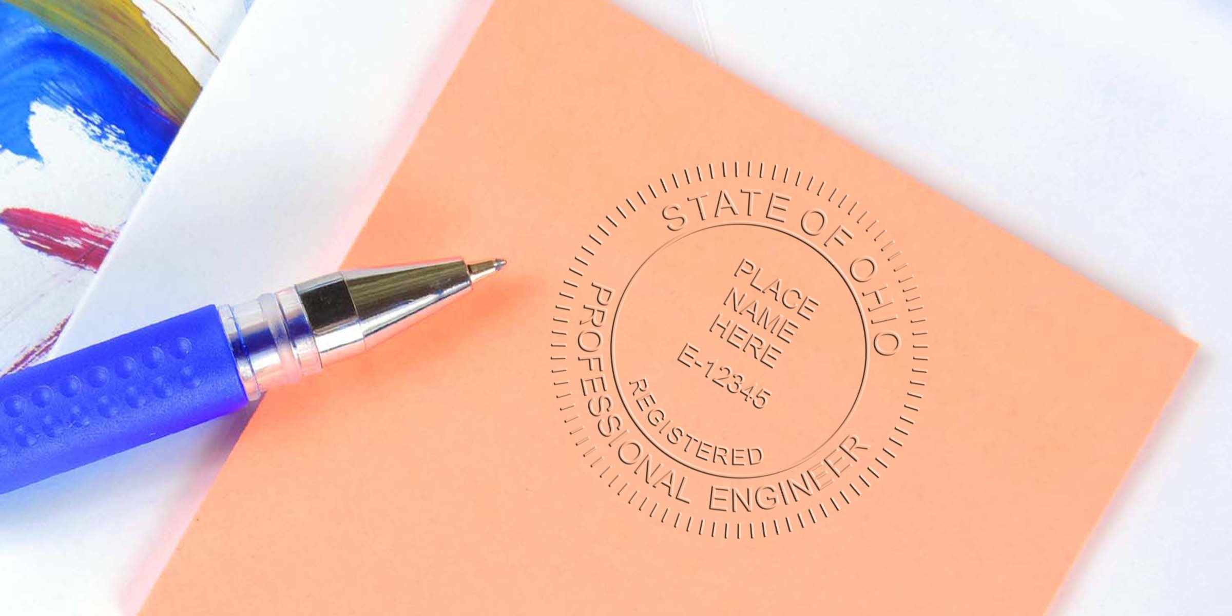 Ohio engineer stamp on orange paper with blue pen, set against a colorful painted background, highlighting Ohio engineer stamp requirements.