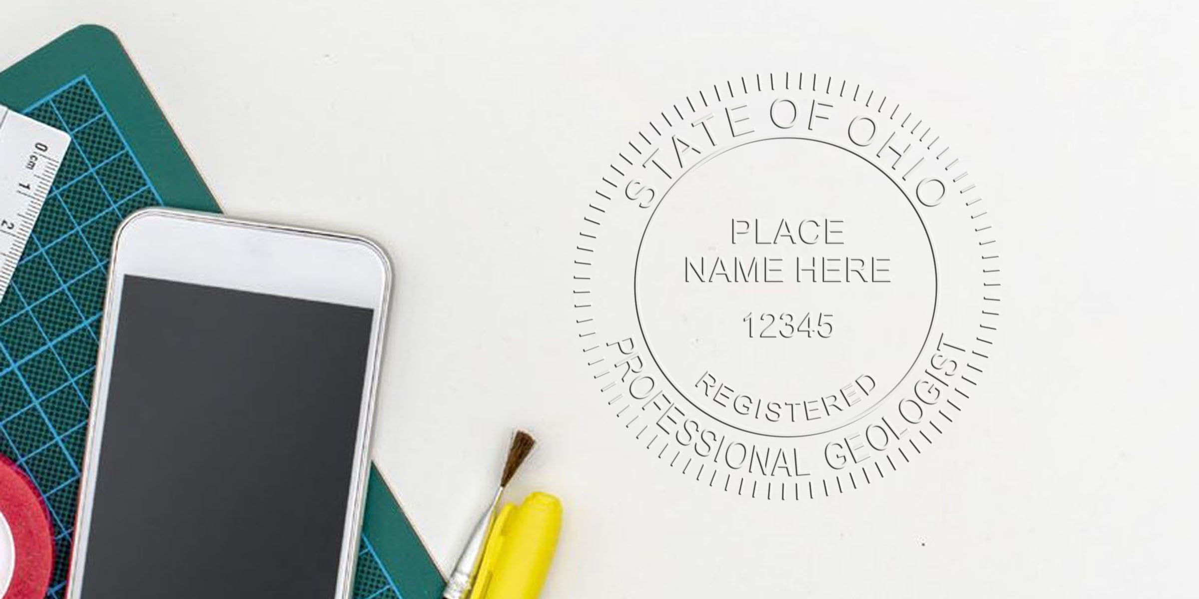 Professional Ohio geologist stamp with smartphone, cutting mat, paintbrush, and highlighter on white desk, meeting geologist seal requirements.