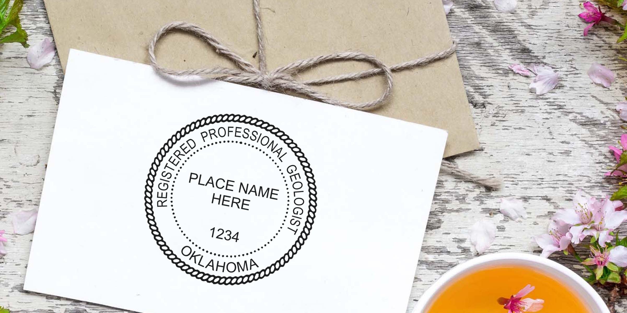 Personalized Oklahoma geologist seal stamped on white card beside brown envelope and floral teacup on wooden table.