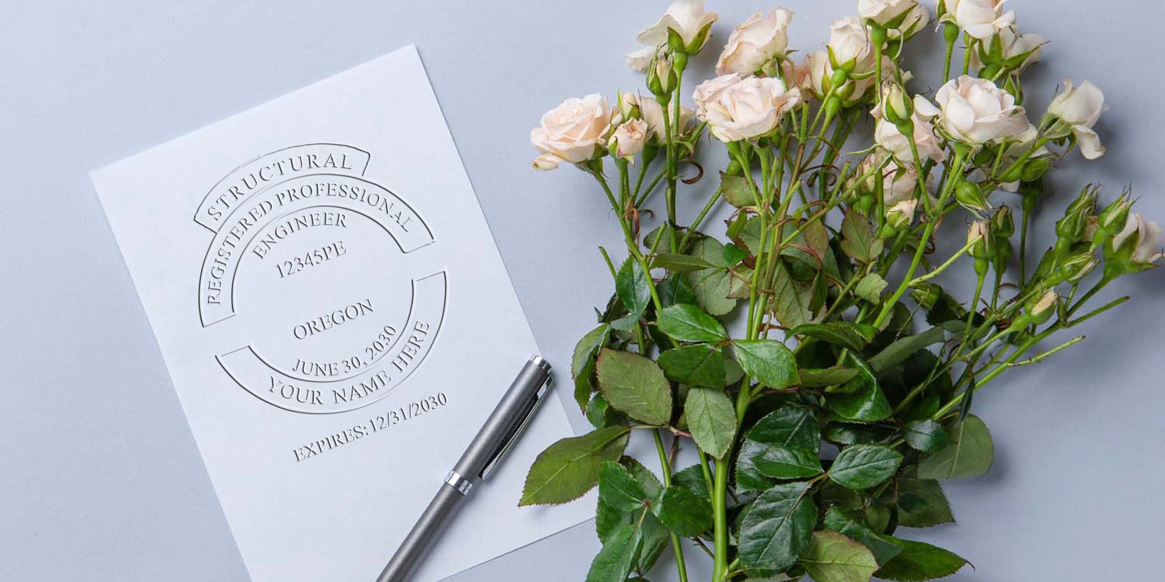 Oregon engineer stamps with a registered professional engineer seal on white paper, alongside a silver pen and white rose bouquet on a gray background.