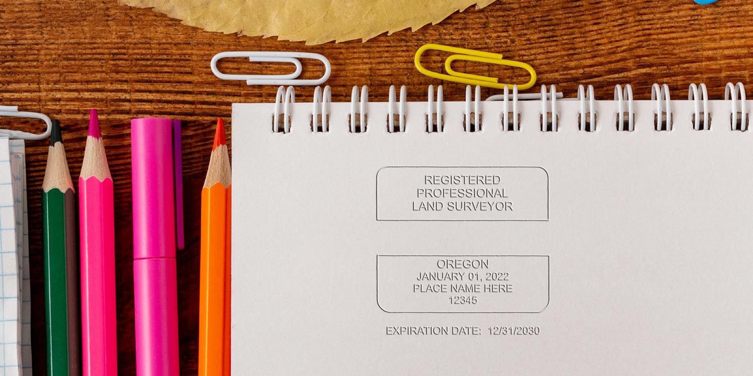 Notepad with Oregon land surveyor stamp, colored pencils, and paper clips on wooden desk showcasing key design elements for certification.