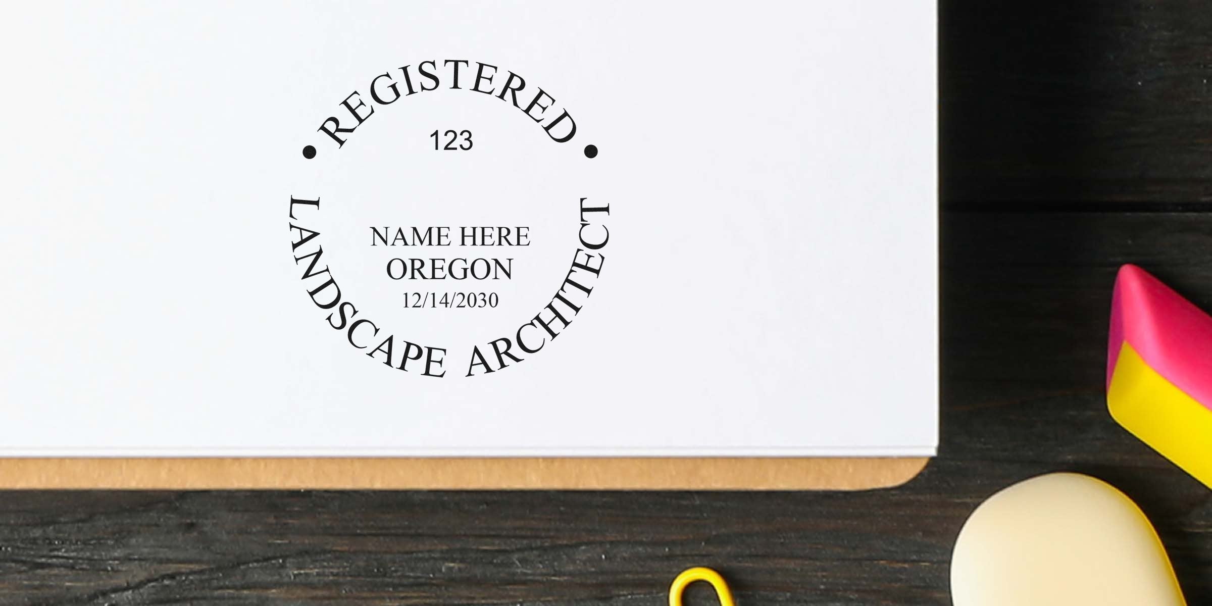 Registered landscape architect stamp on white paper with office desk items, illustrating Oregon landscape architect rules and seal requirements.