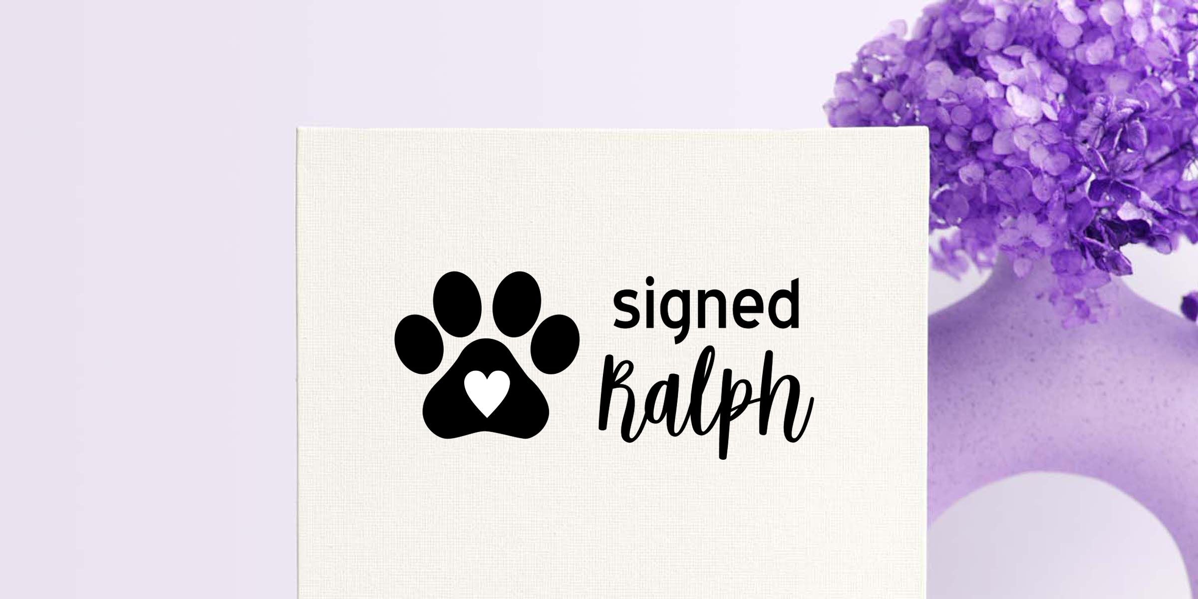 White pet sympathy card with black paw print heart logo and “signed Ralph” text on a lavender floral background