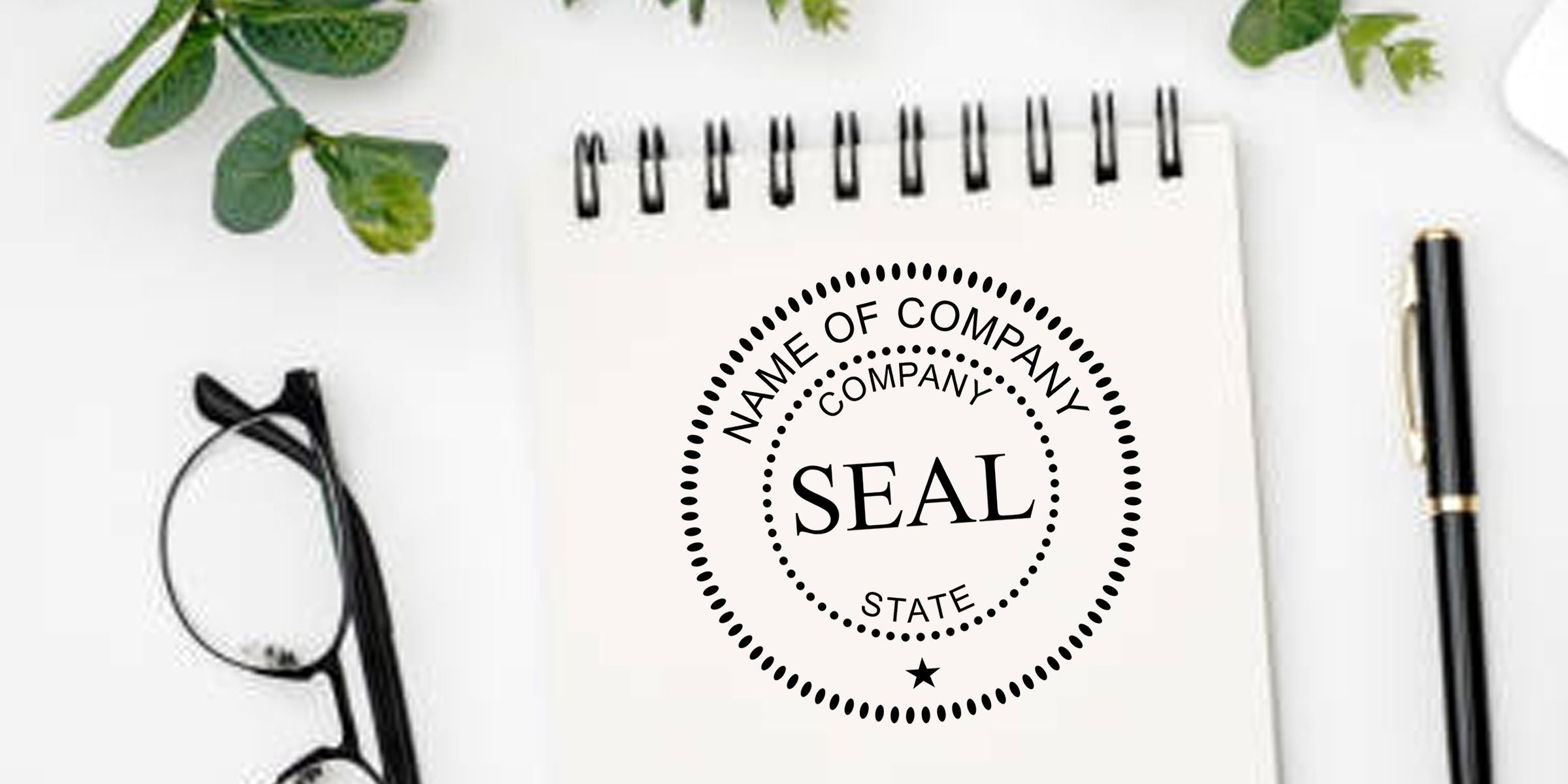 Custom company seal logo mockup on a spiral notebook with pen, eyeglasses, and greenery on a white desk, business branding template.