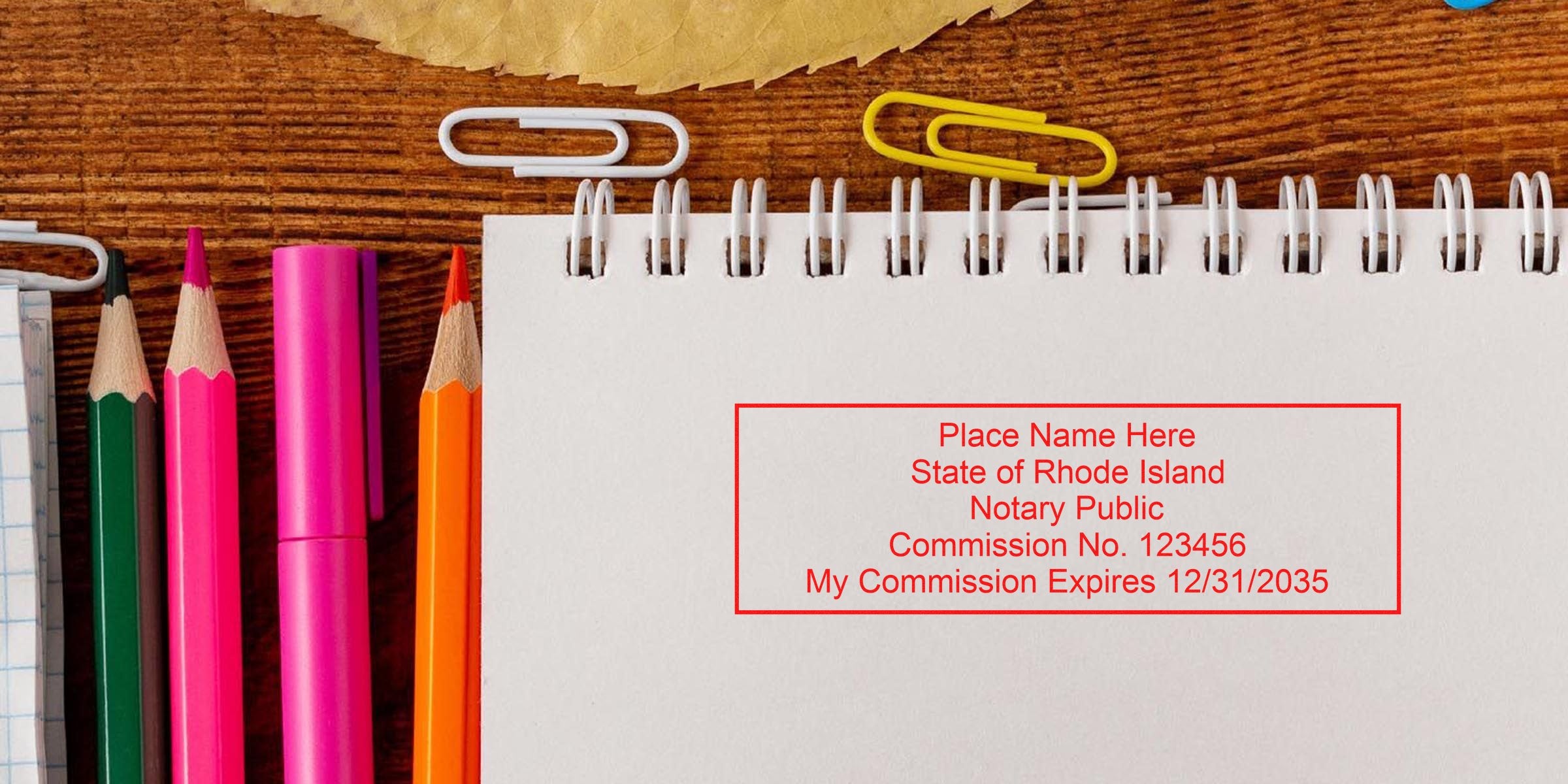 Rhode Island notary stamp on white spiral notebook with colored pencils and paper clips on wooden desk, showing the official notary seal guide.