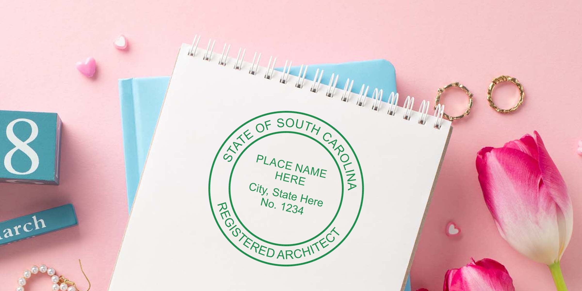 South Carolina architect seal stamp on notebook with pink tulips and gold rings on pink background, highlighting SC architect stamp cost and fees.