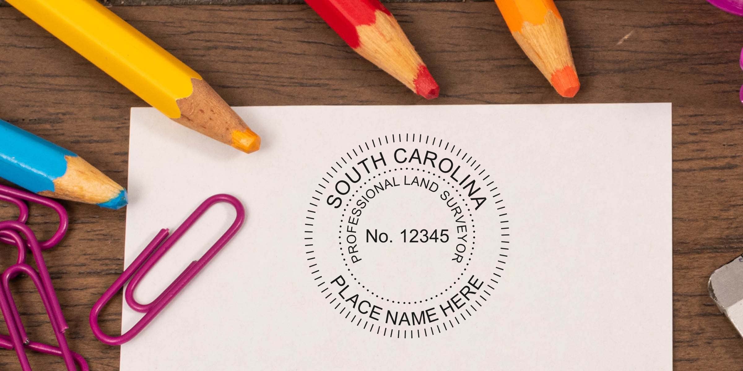 South Carolina land surveyor seal stamped on paper, surrounded by colorful pencils and purple paper clips on a wooden desk, showcasing land surveyor embosser choice.