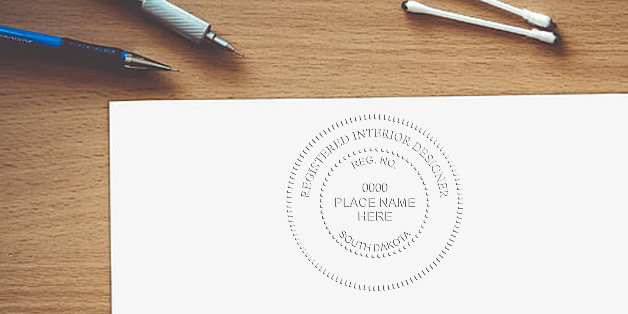 Registered interior designer embossed seal on white paper with pens and cotton swabs on wooden desk, showing South Dakota interior designer license and stamp requirements.