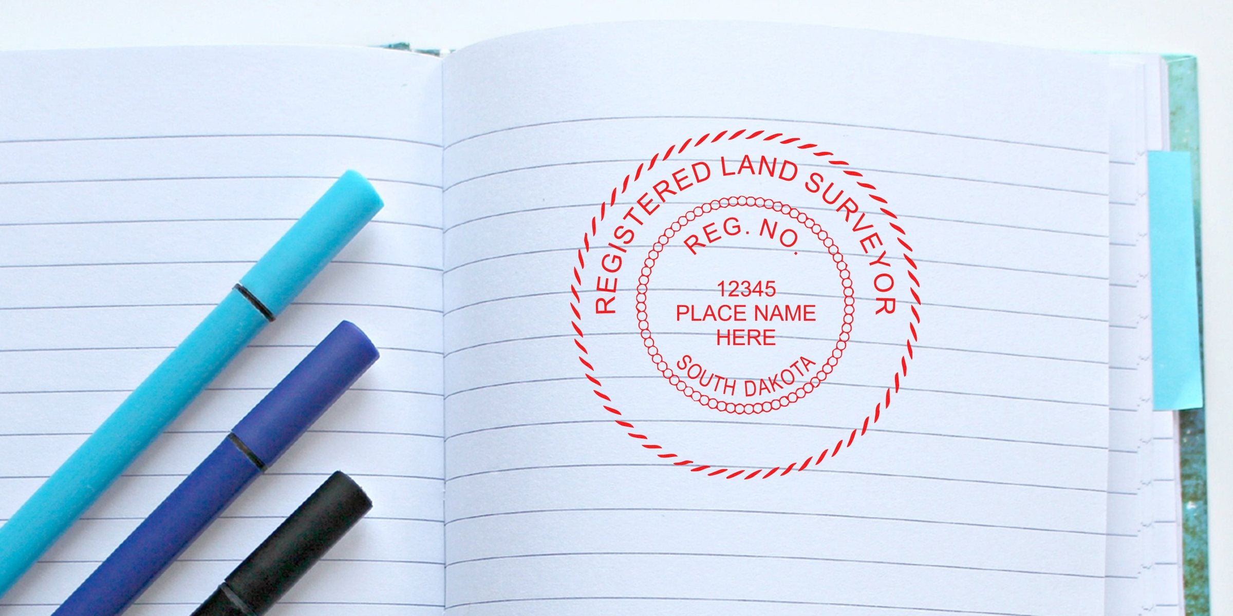 South Dakota land surveyor seal stamped on lined notebook with blue and black pens, showing embosser guide for land surveying services.