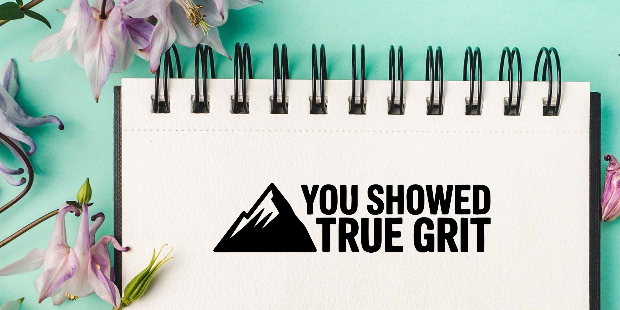 Notebook with “You Showed True Grit” motivational text and mountain icon on a teal floral background with purple flowers