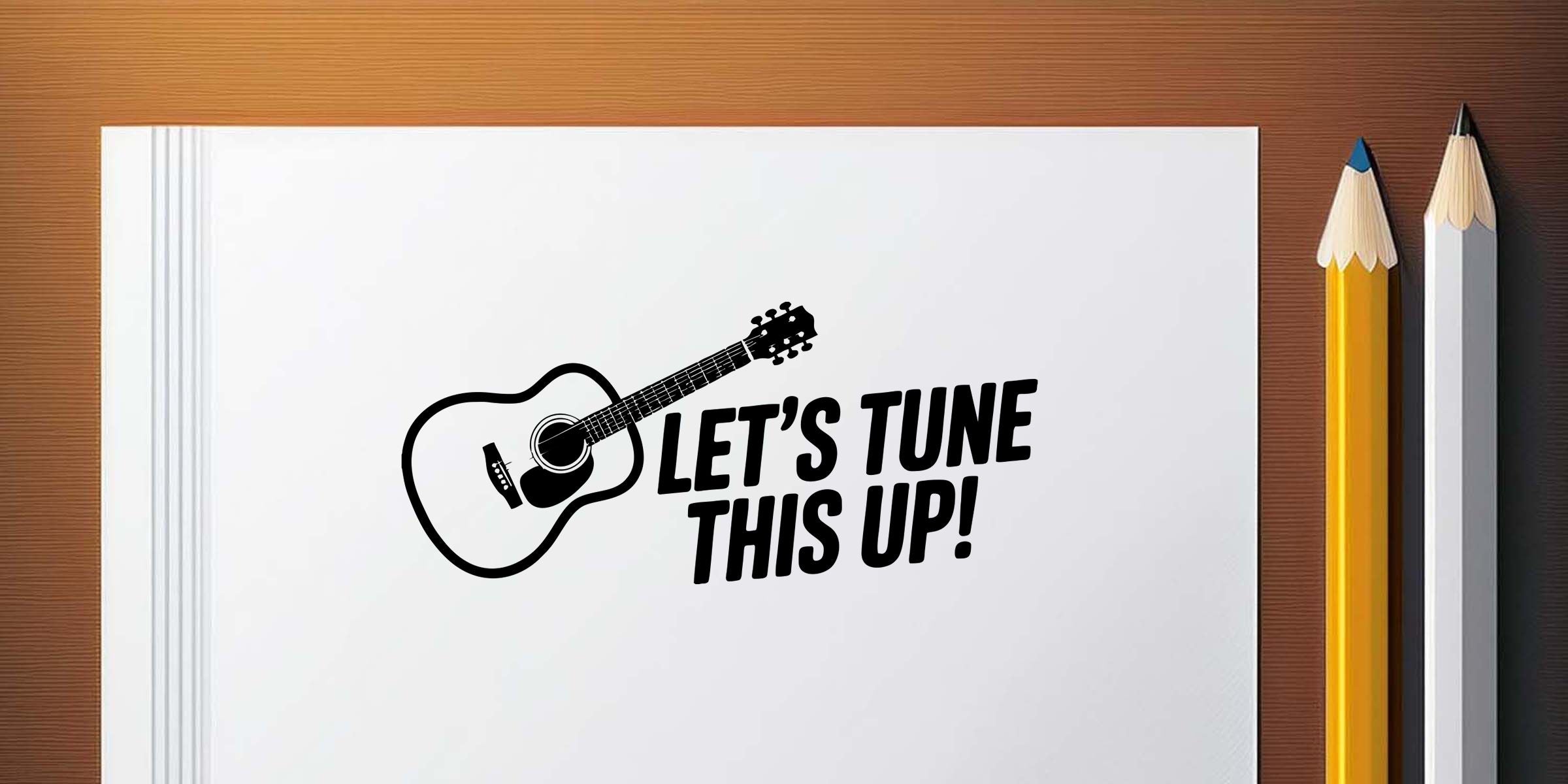 Open notebook with guitar graphic and bold “Let’s Tune This Up!” text beside pencils on a wooden desk for music lesson and songwriting themes