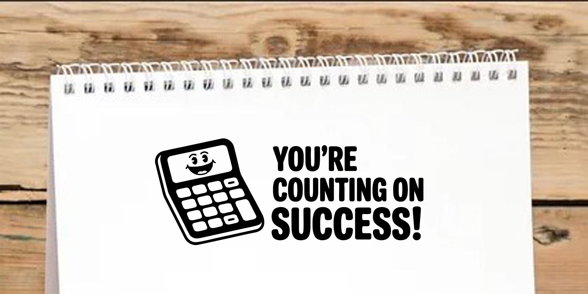 Notebook on a wooden table with a smiling calculator graphic and bold text reading “You’re counting on success!”