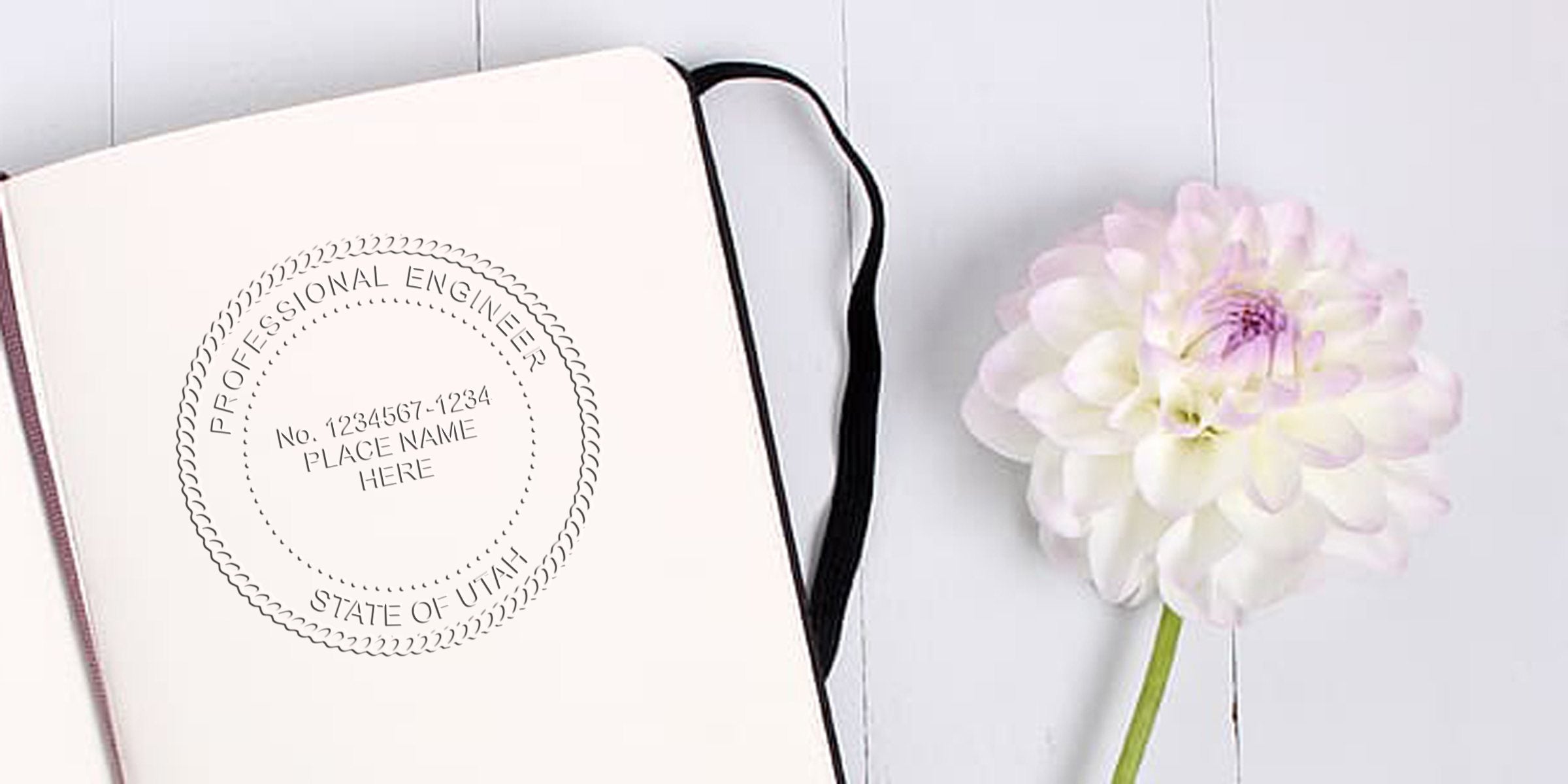 Custom engineer stamps, including Utah engineer stamp, on a notebook beside a white flower on a wooden table.
