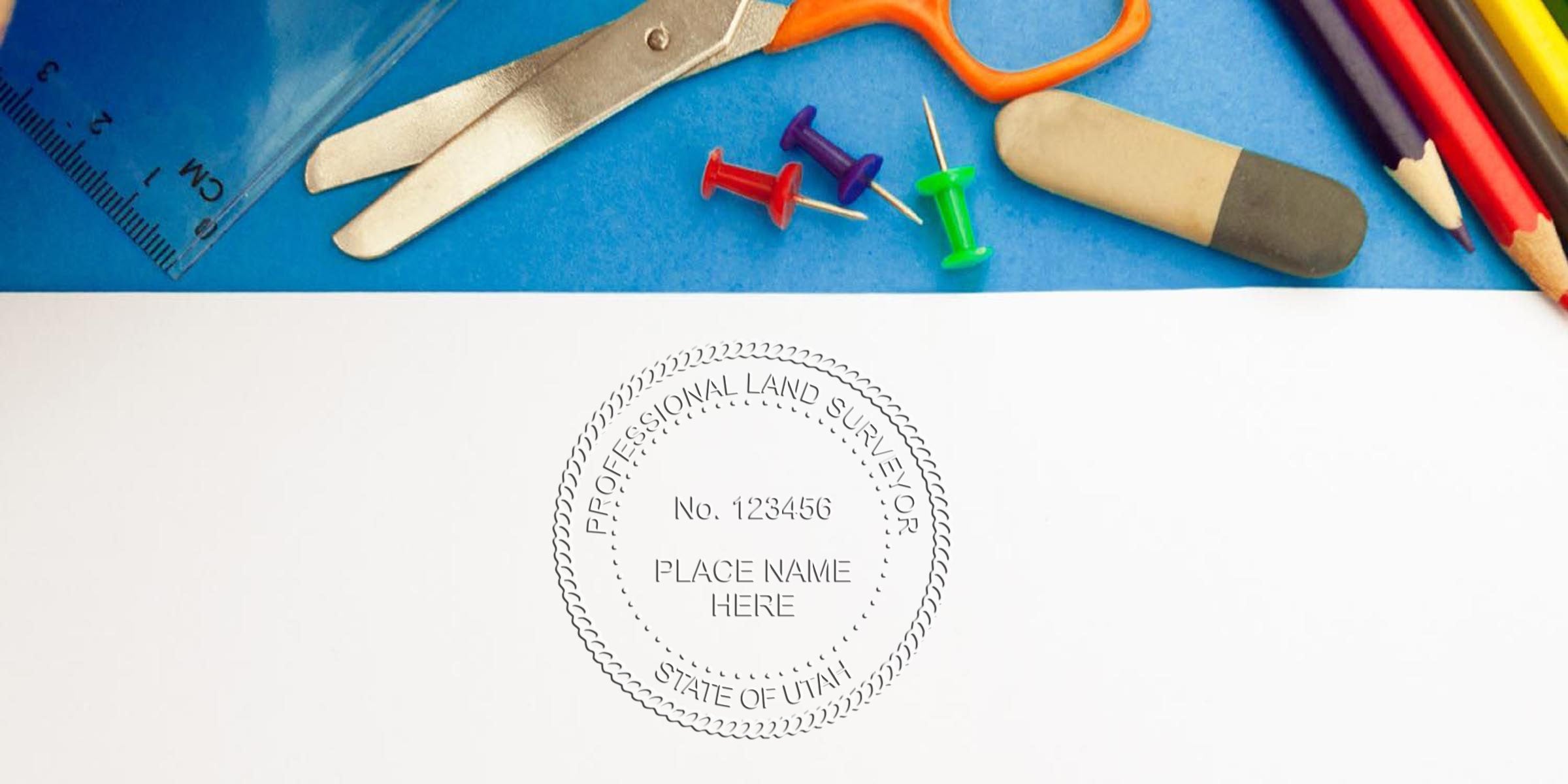 Utah land surveyor stamp on paper, surrounded by office supplies: ruler, scissors, push pins, eraser, and colored pencils, all set on a blue background.