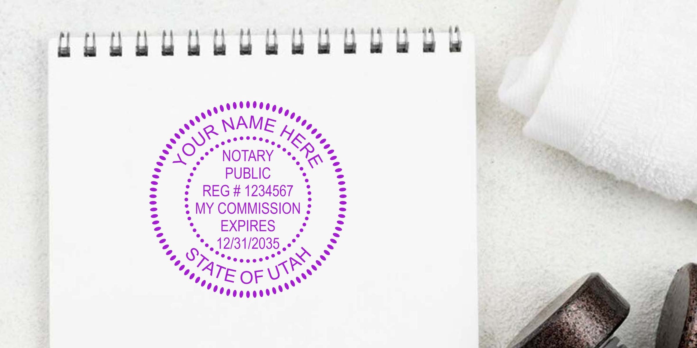 Custom Utah notary stamp with personalized name and commission details on white notebook, showing Utah notary seal expiration and renewal information.
