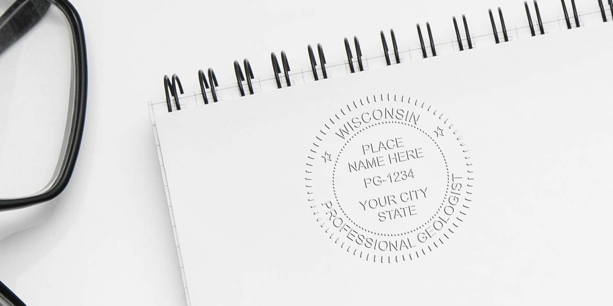 Close-up of Wisconsin geologist seal specs stamped on a white spiral notebook beside eyeglasses, showing a professional geologist certification seal.
