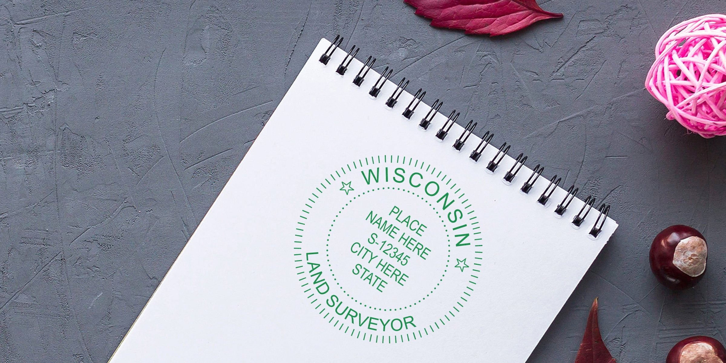 Wisconsin land surveyor stamp on spiral notebook with autumn leaves and chestnuts on gray background, emphasizing land surveyor fees and stamp cost budgeting.