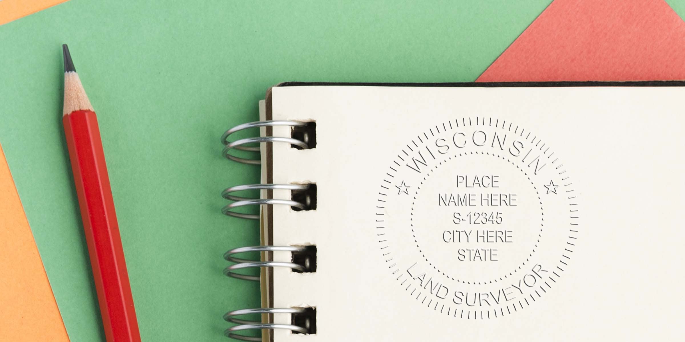Red pencil next to spiral notebook with Wisconsin land surveyor stamp on colorful paper, emphasizing the stamp's size.