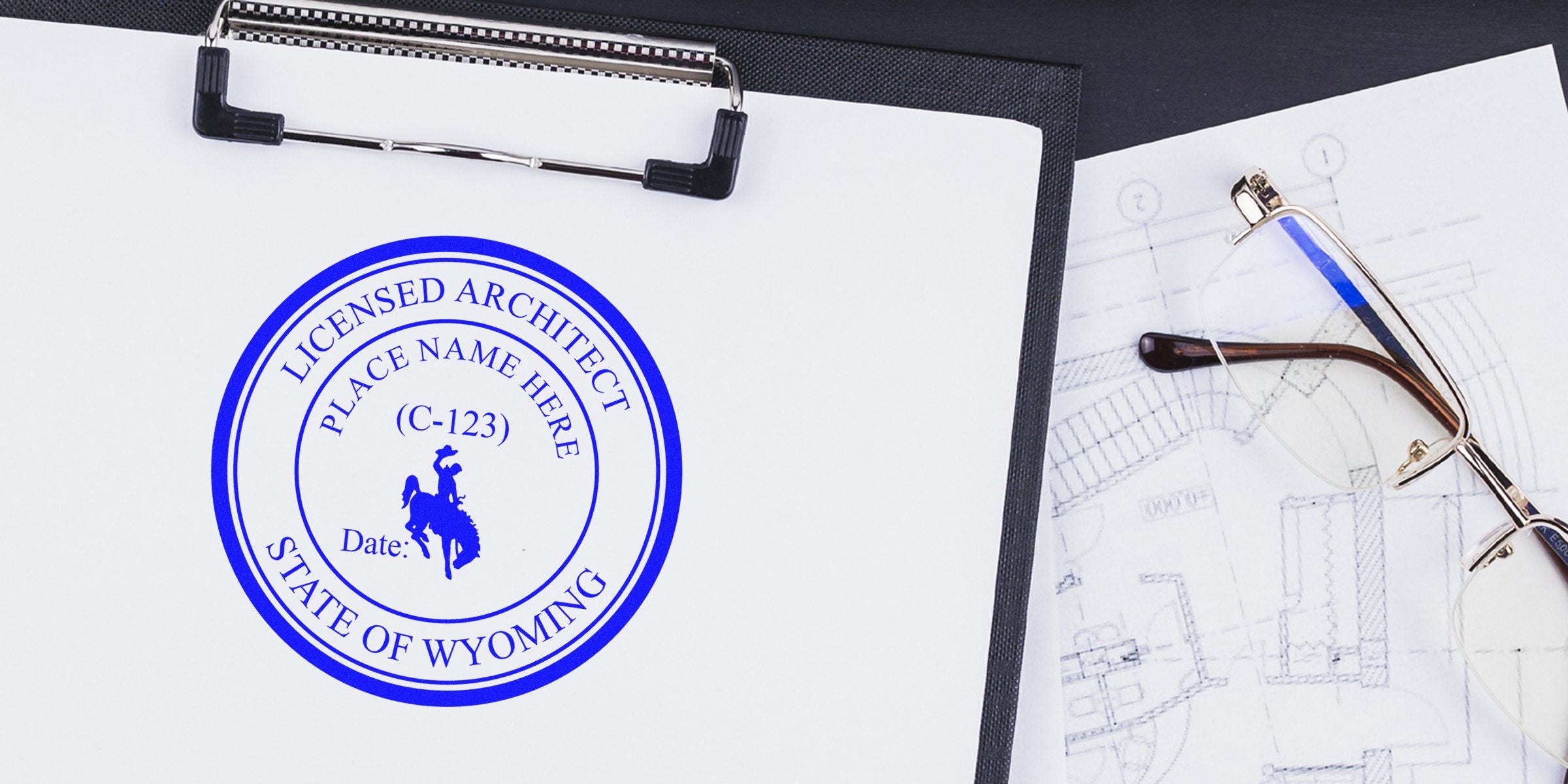 Wyoming architect stamp on clipboard with blueprint and glasses, showing Wyoming architect license seal; purchase Wyoming architect stamp.
