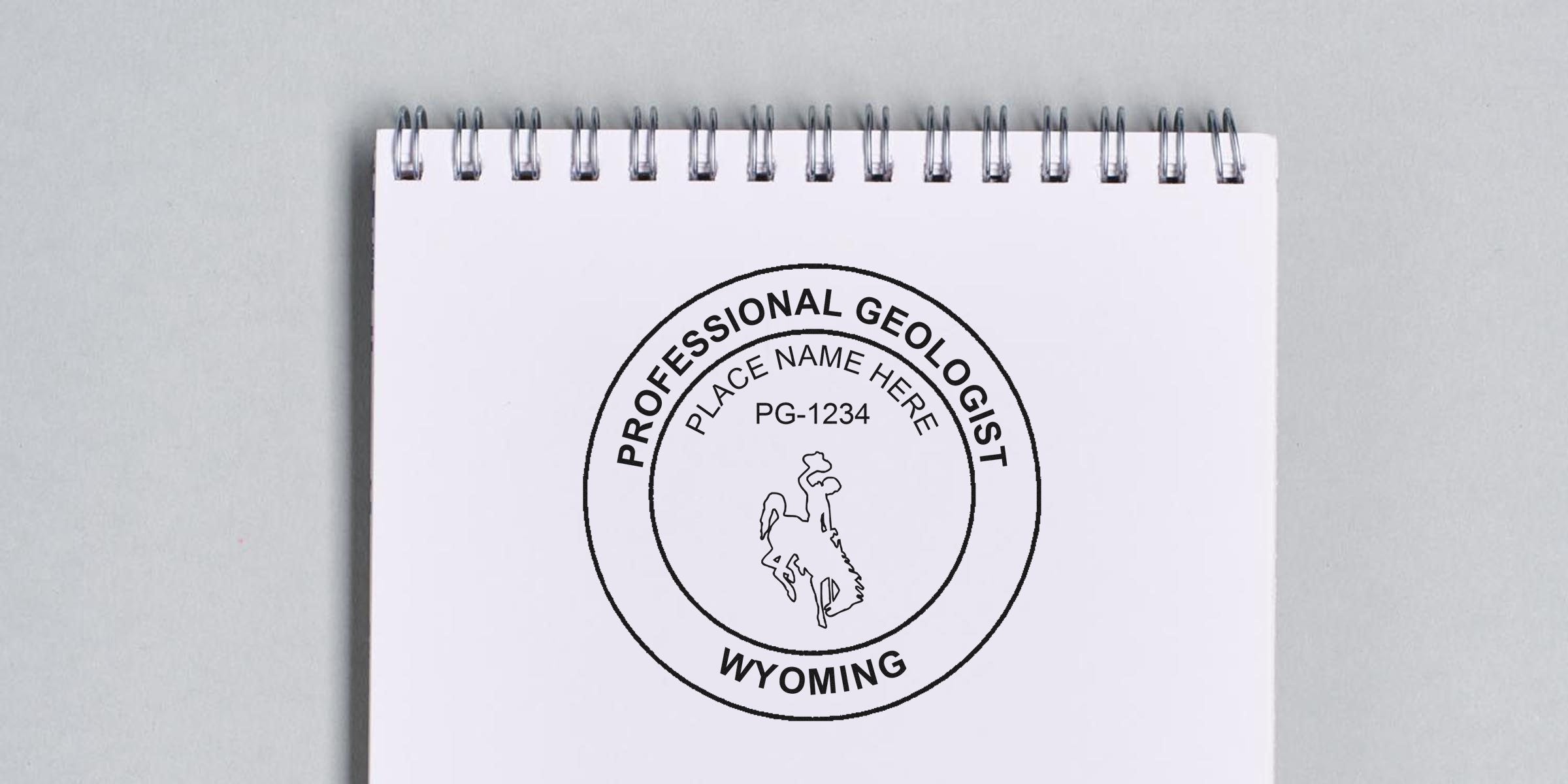 Wyoming geologist stamp design on white spiral notebook with cowboy on horse illustration and license number PG-1234, compliant with geologist stamp standards.