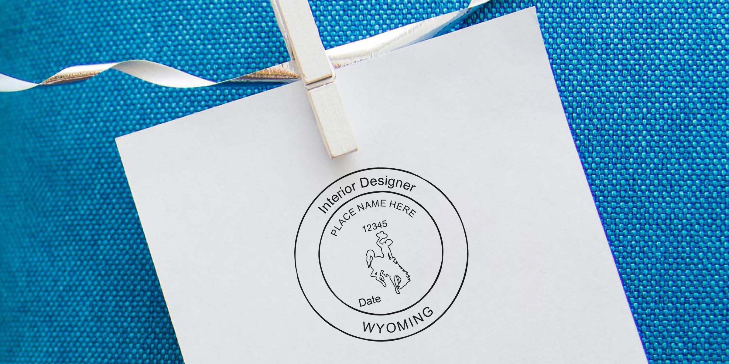 White paper with Wyoming Interior Designer Seal on blue textured background, hanging by clothespin, symbolizing Interior Designer Seal Application.